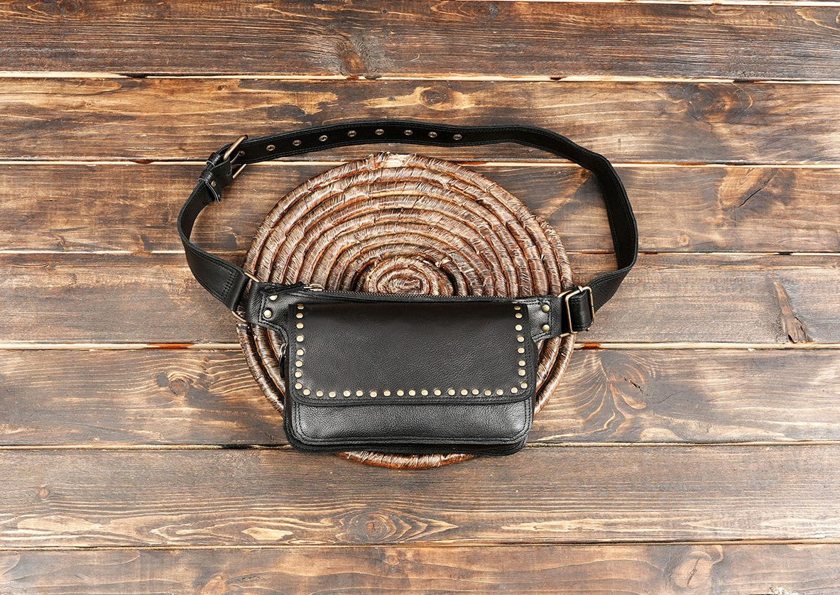 Handmade black leather belt bag with brass studs on wooden background