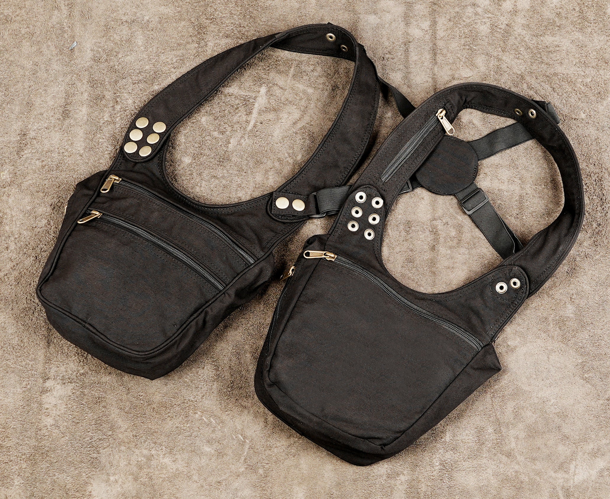 A pair of black industrial-style shoulder bags with multiple zippered pockets, metal grommets, and snap buttons, 