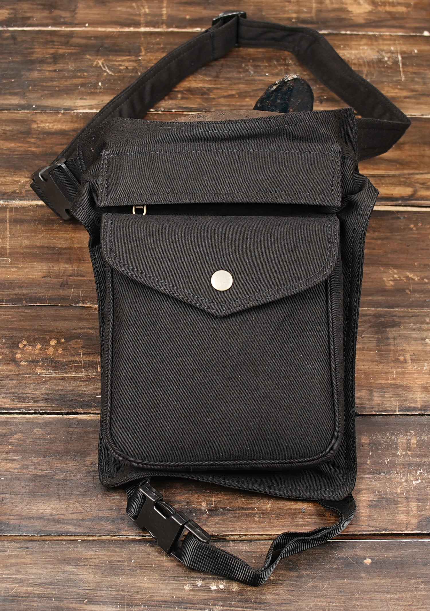 Made from durable black cotton, it features a spacious front pouch with snap-button closure, perfect for carrying your essentials like phone, wallet, and keys while keeping your hands free.