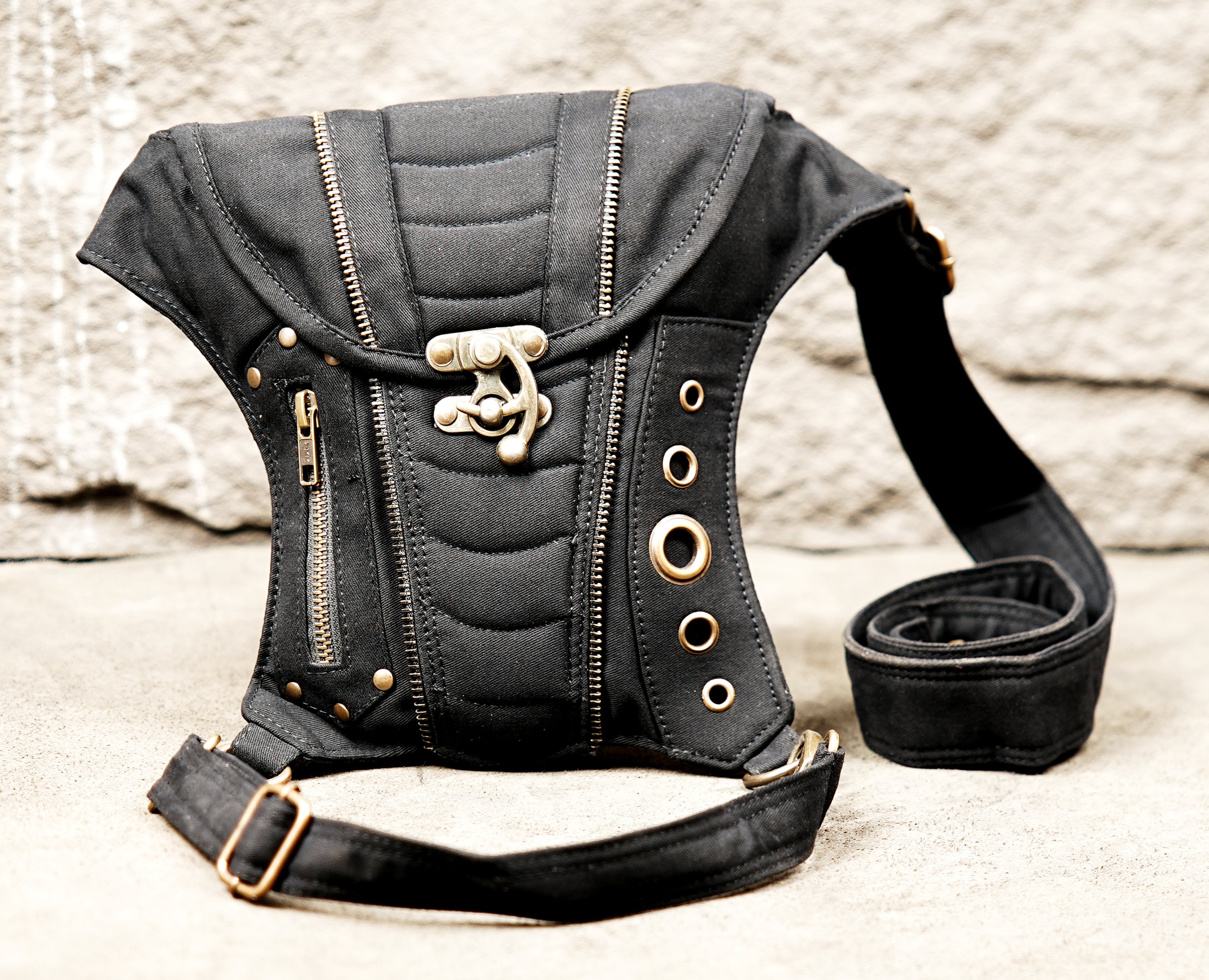 Multi-pocket cotton thigh bag with studded metal hardware on natural wood backdrop.