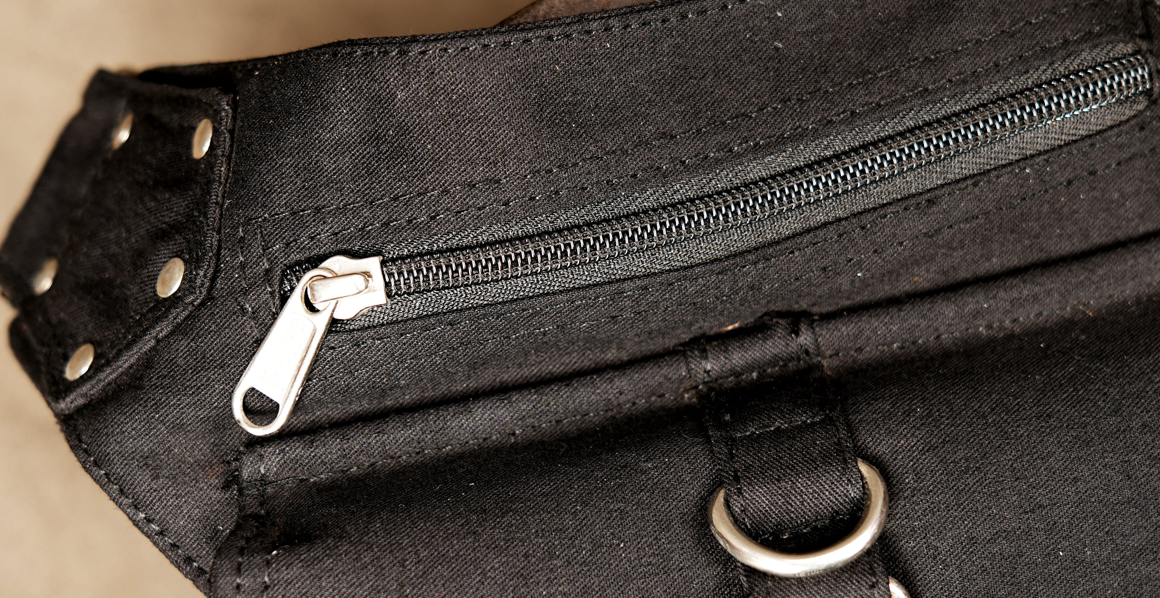 The main compartment of the black bag is secured by a sturdy horizontal metal zipper.
