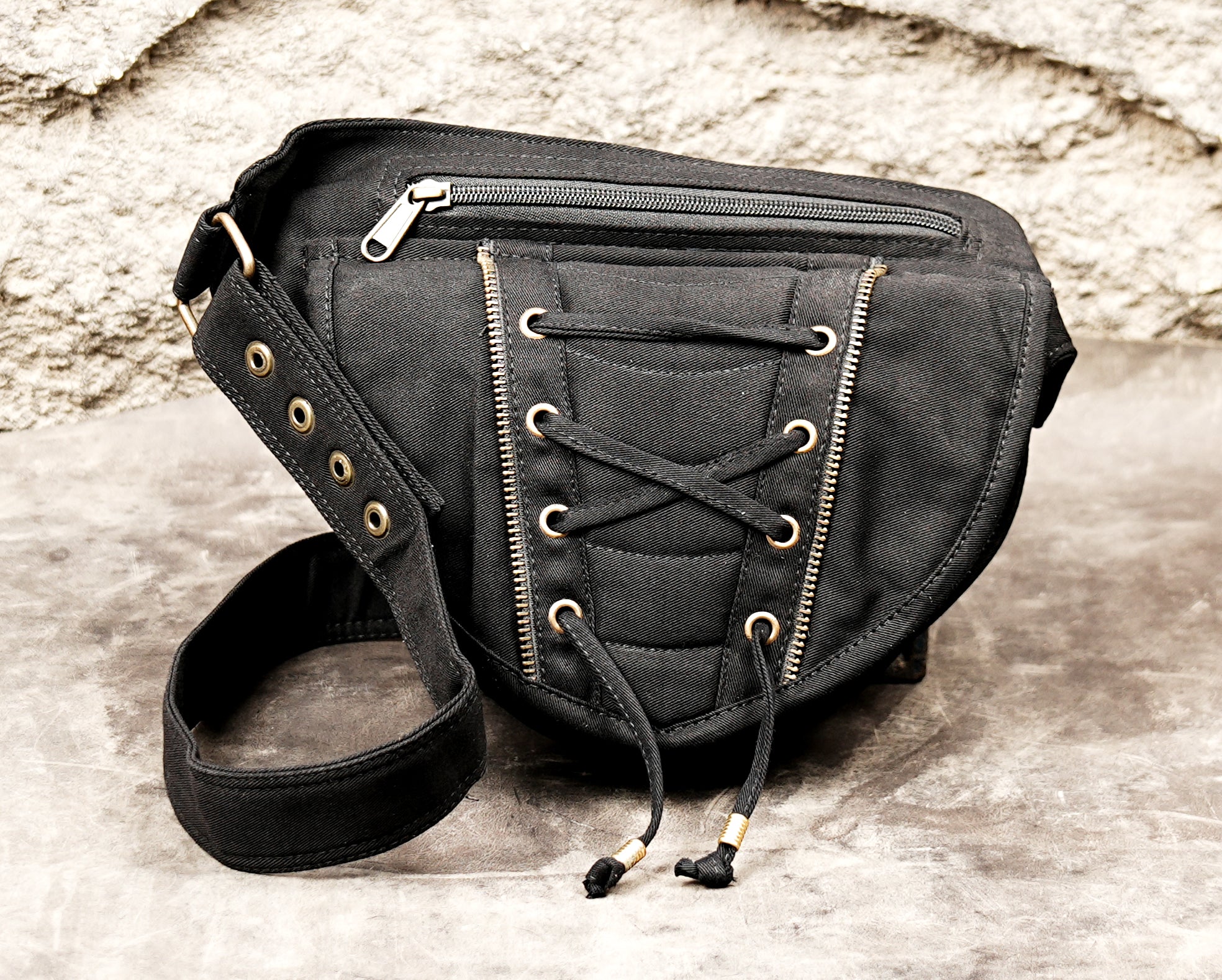 Close-up view of a black cotton canvas utility belt bag showing the distinct corset-style lace-up front pocket and two adjacent silver-tone zippers.
