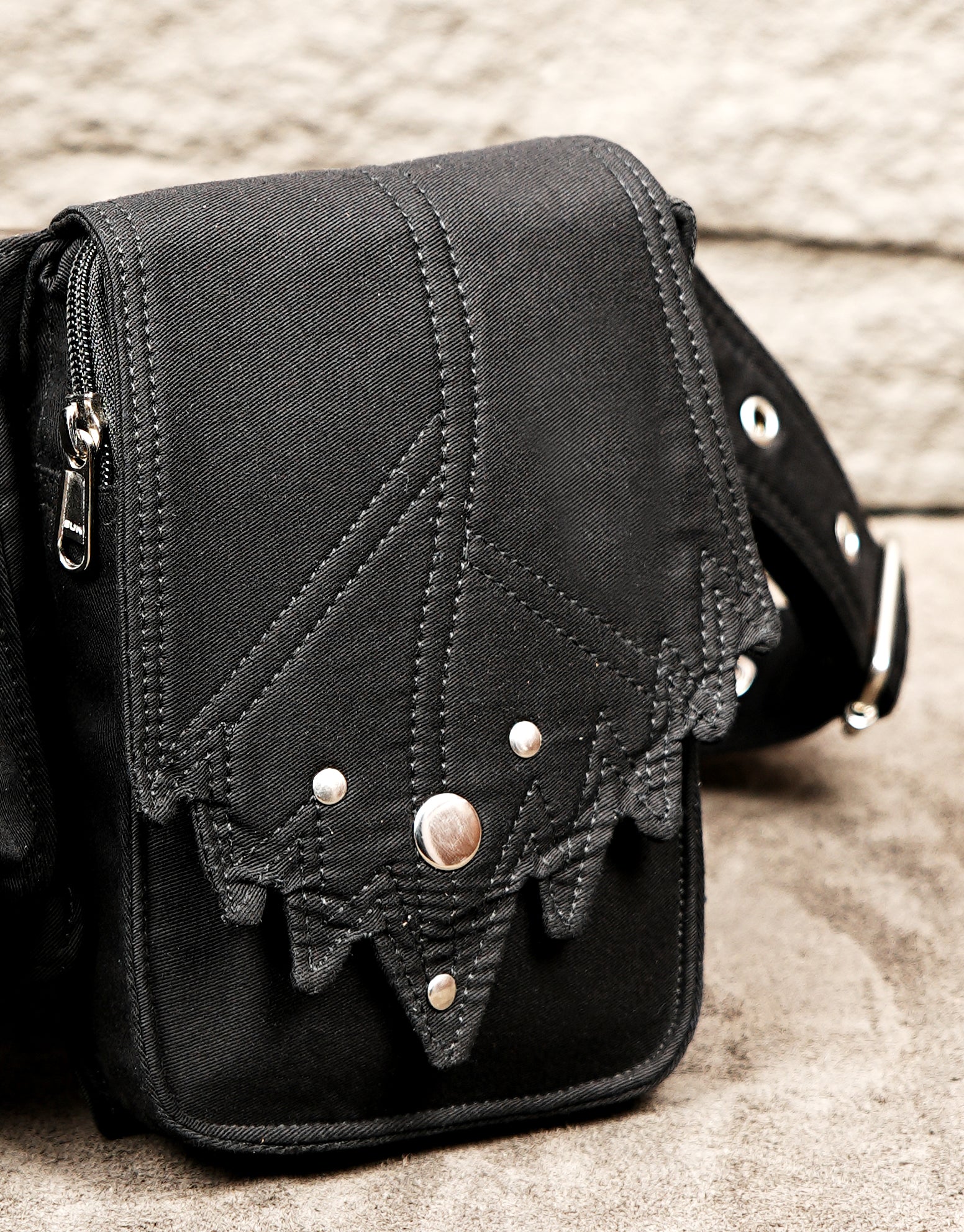 Leather-style black hip bag with attached studded waist strap and blue stone detail.