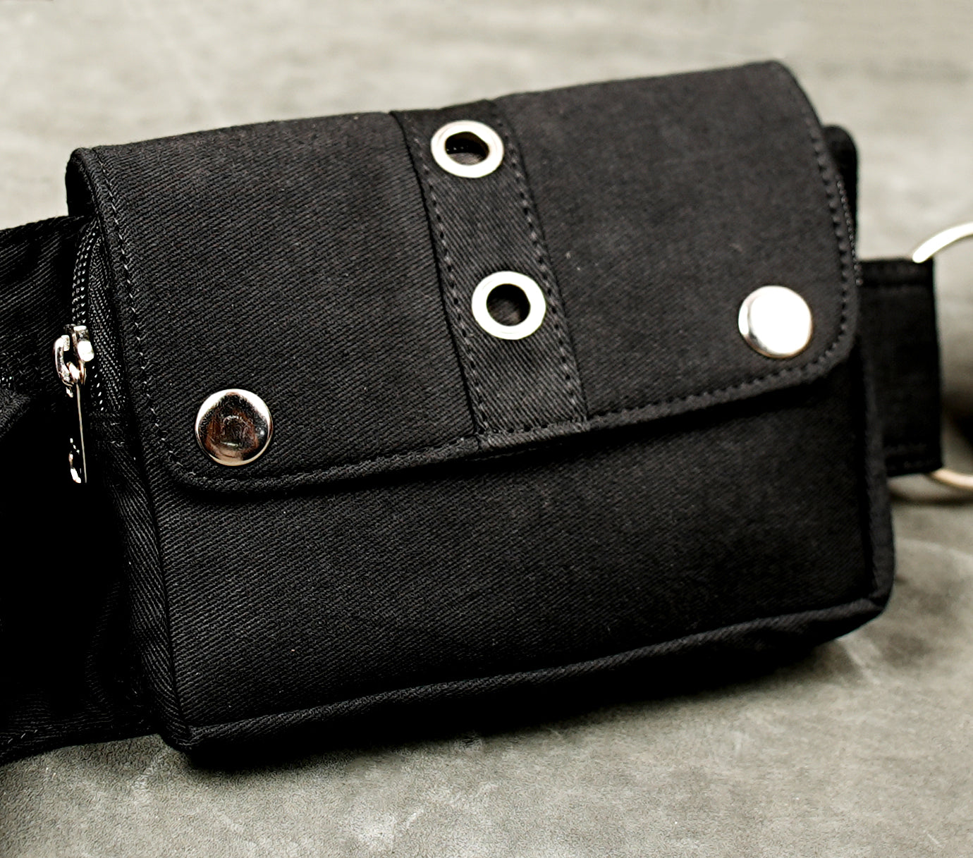 Black cotton utility belt with front zip pocket and studded storage pouches for outdoor adventures.