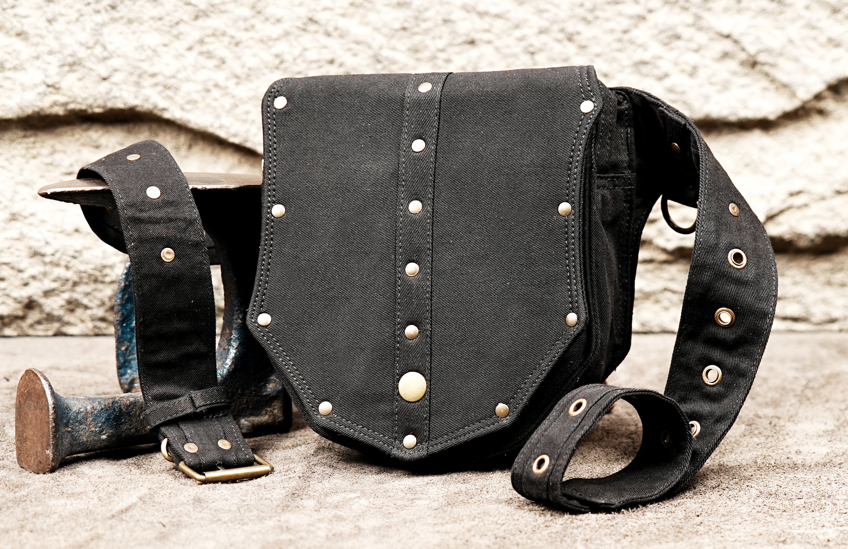 The front of a black cotton festival belt bag, highlighting the row of small round brass rivets and the larger central rivet detail.