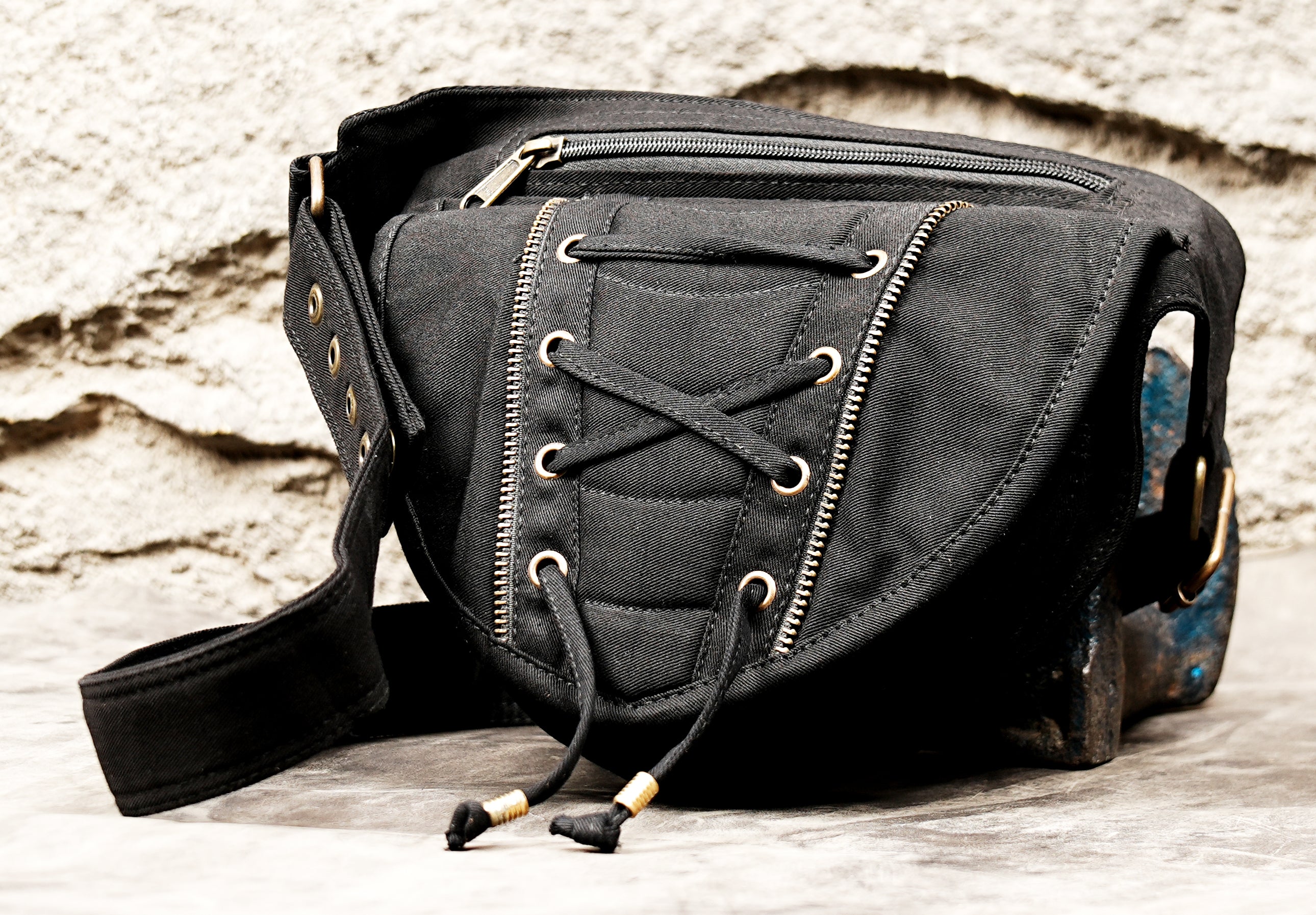 The front of a black cotton festival belt bag highlighting the metal eyelets, black cord lacing, and zipper teeth design.