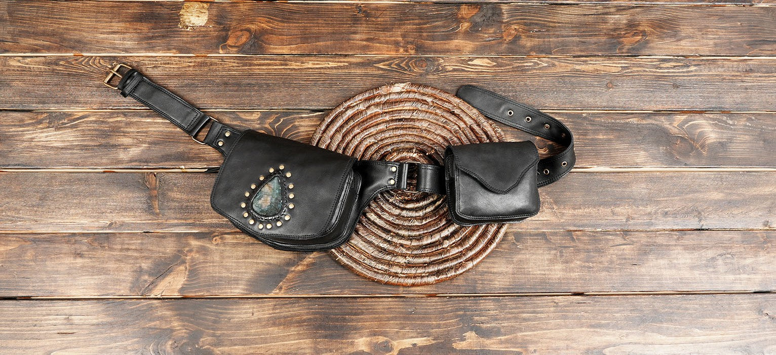 Handmade black leather belt bag with gemstone accent on wood background