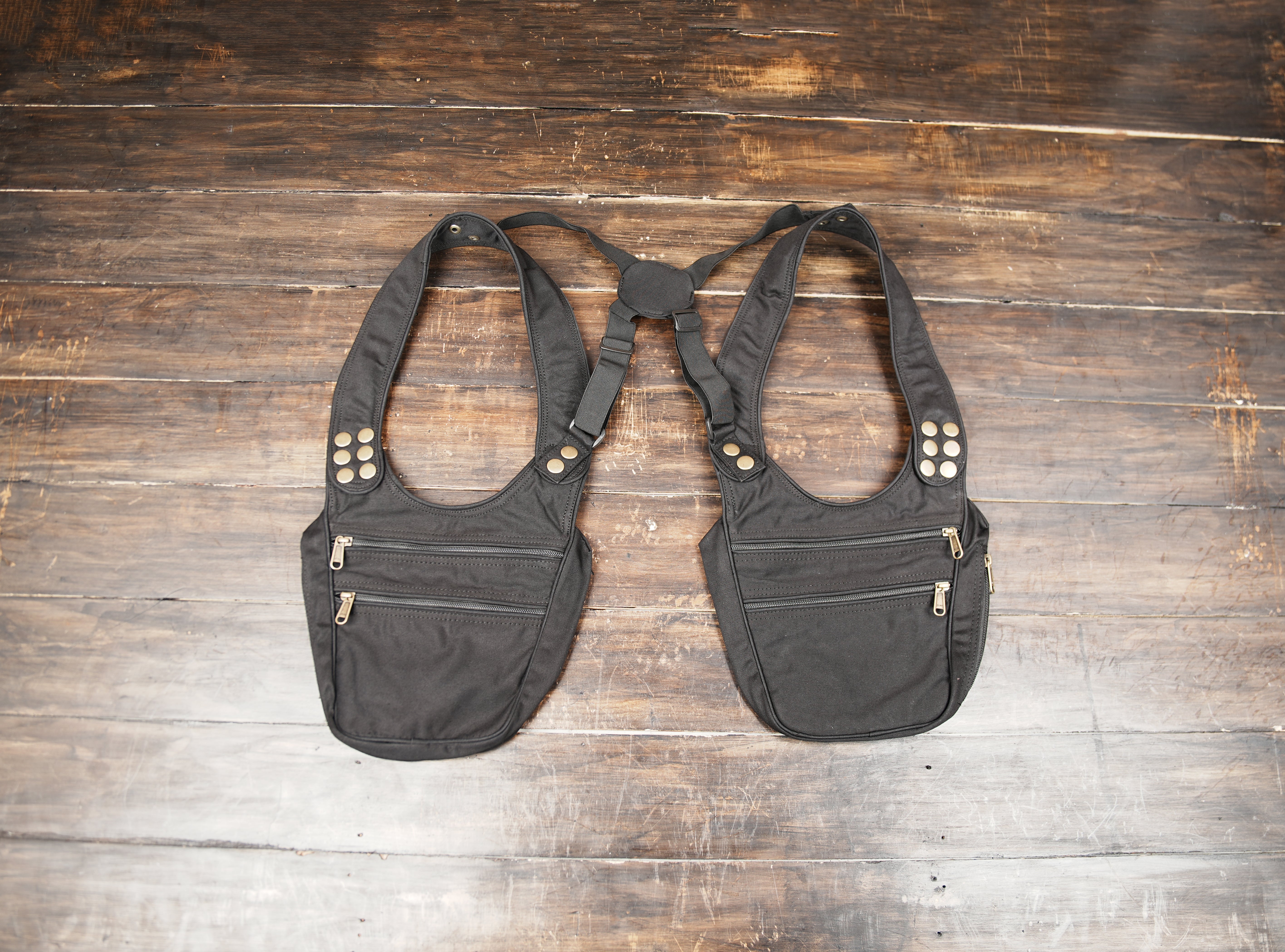 Black cotton holster bag with dual zipper pockets displayed flat on wooden background