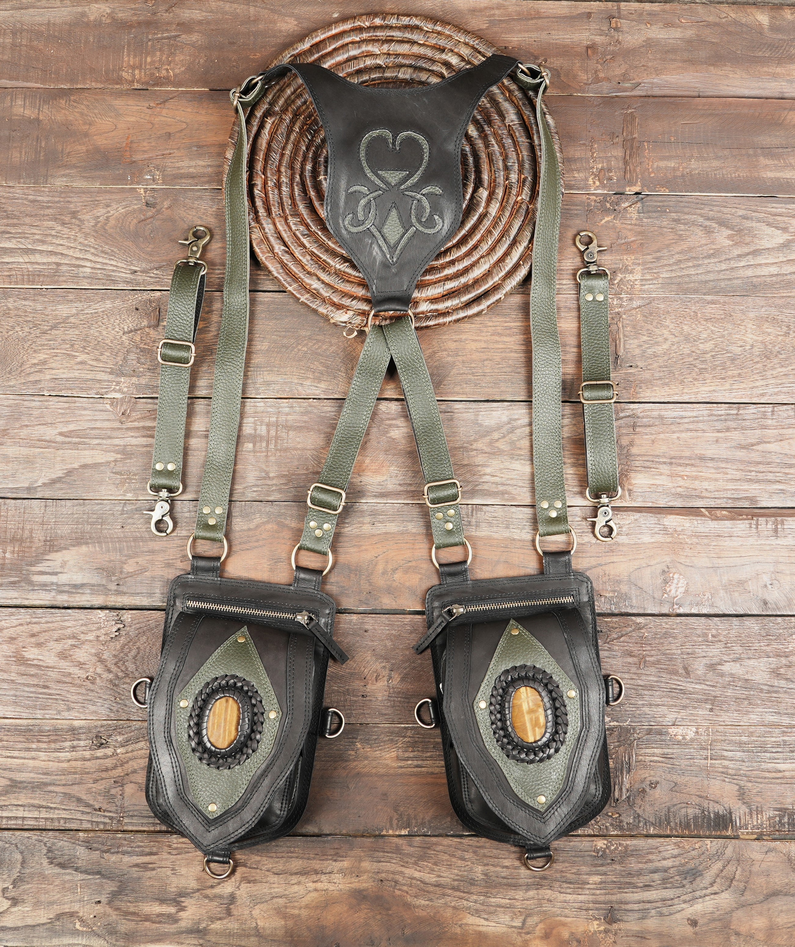Black leather dual holster bag with olive green straps and gemstone accents on wooden background.