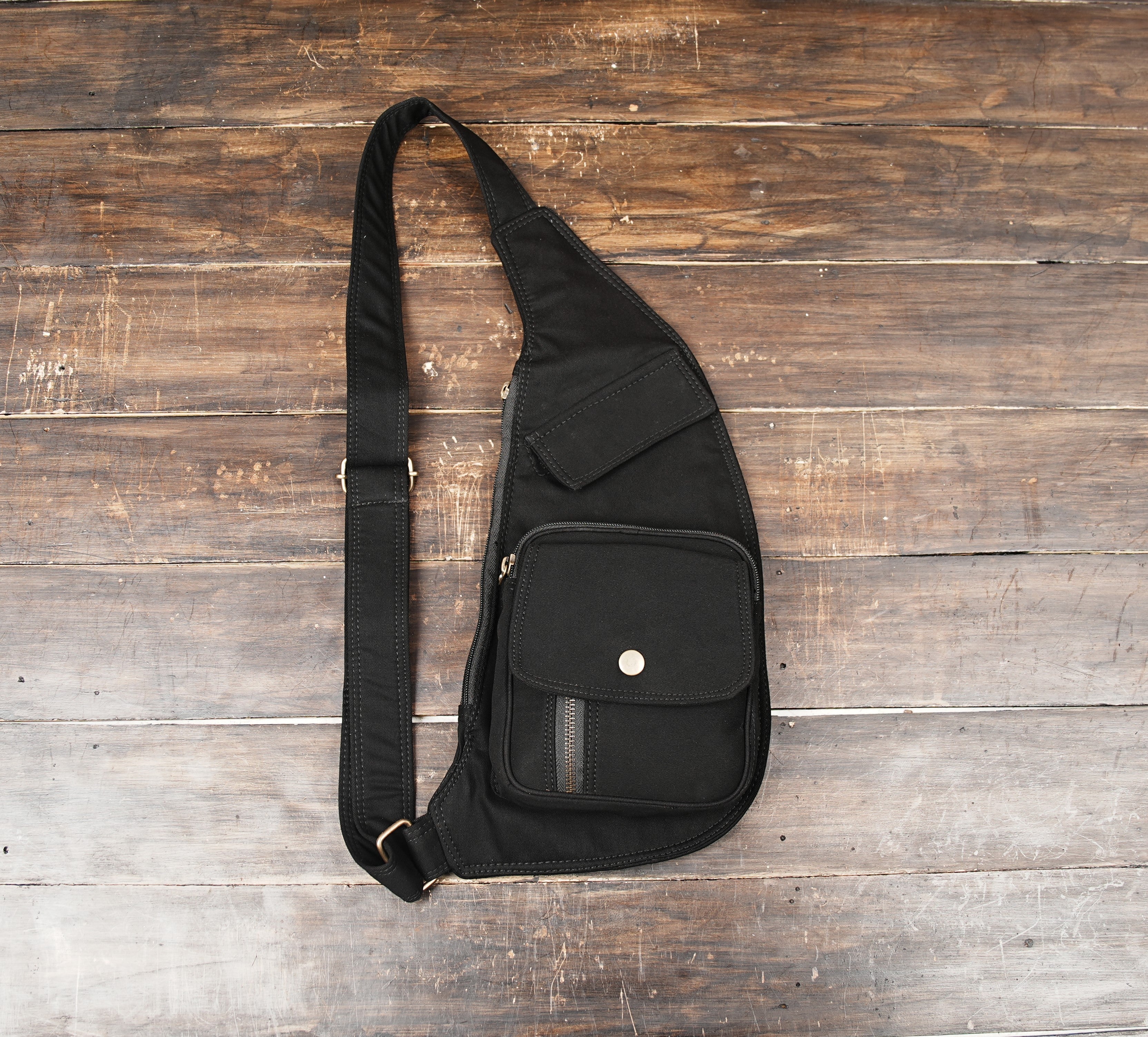 Black cotton holster bag with adjustable crossbody strap on wooden background