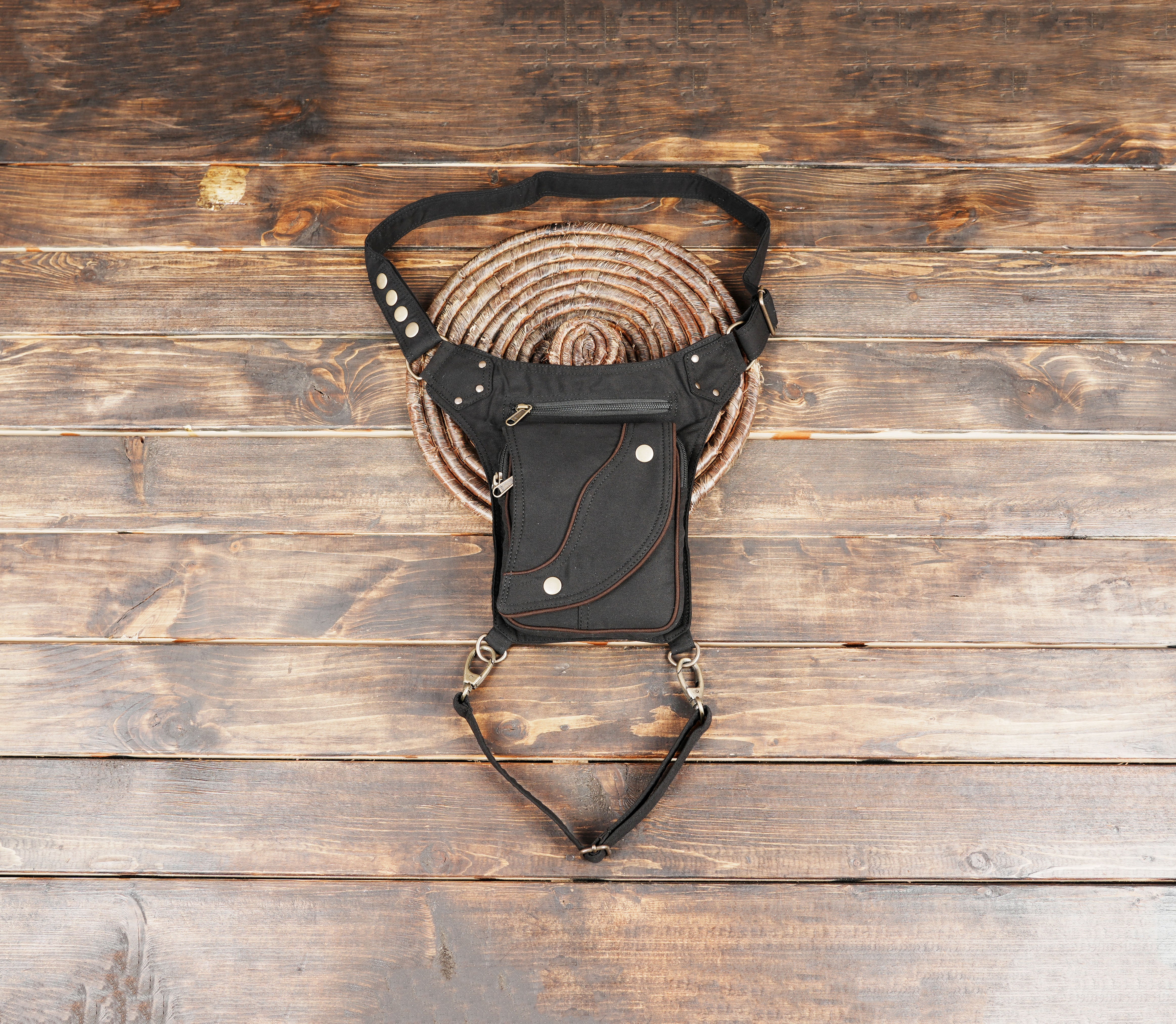 Handmade cotton canvas drop leg bag with curved flap design laid on a dark wood background.