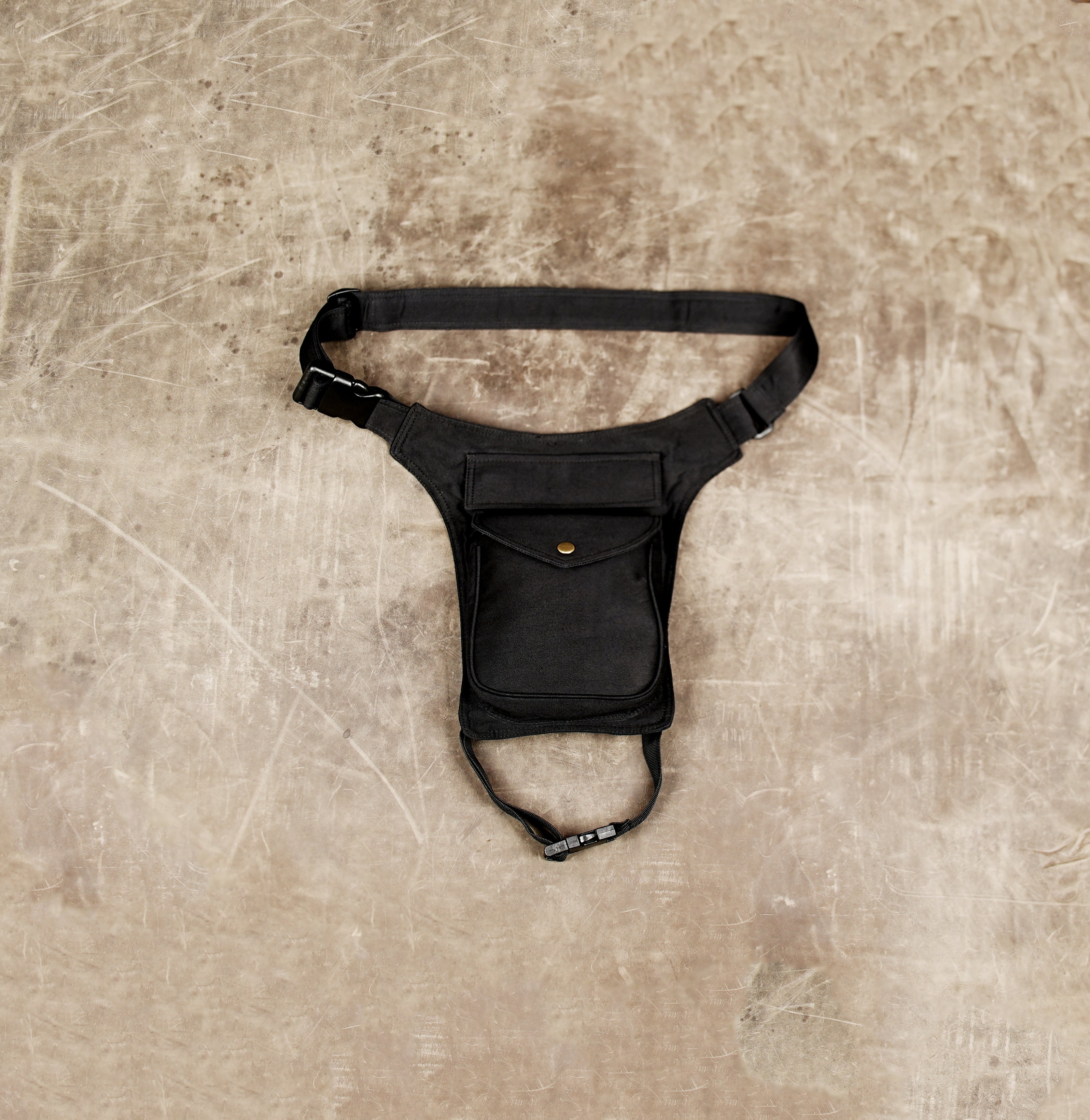 Black thigh bag with flap pocket, brass snap button, and quick release buckle