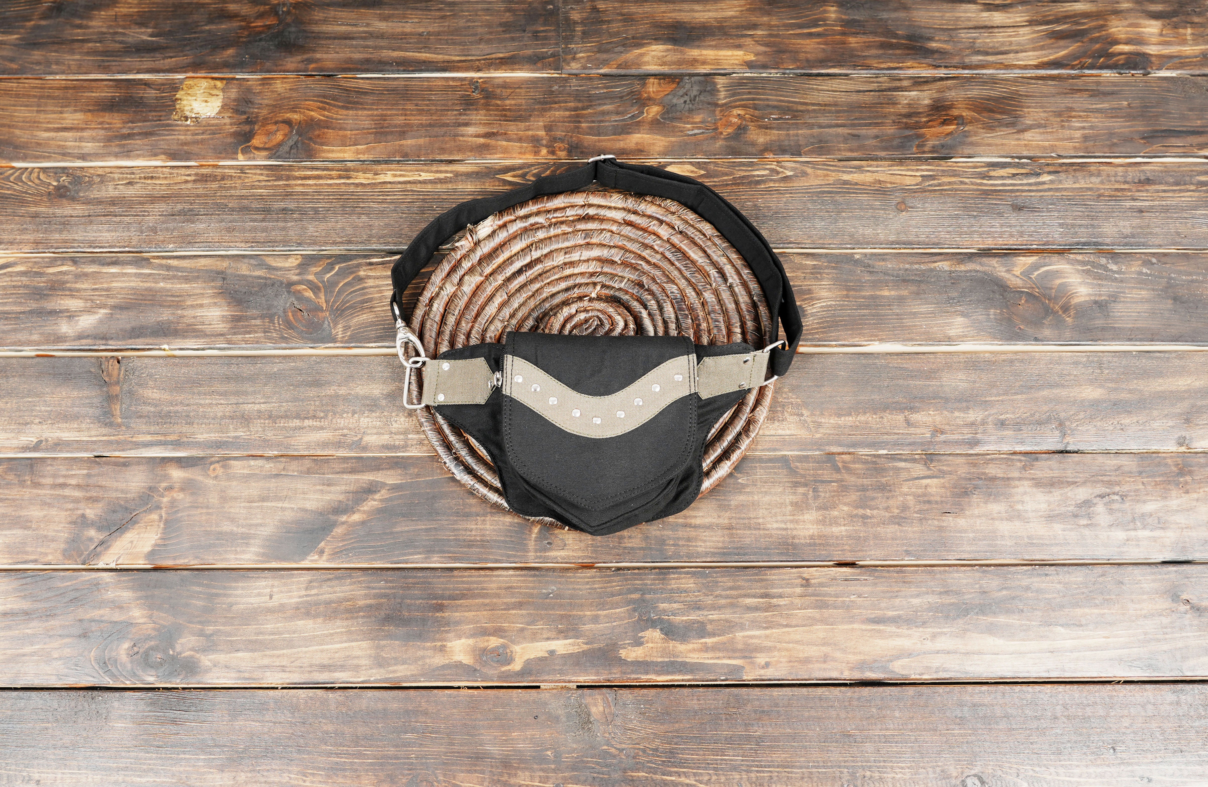 A black cotton utility bumbag with rustic woven trim, laid flat on a weathered wood table for an alternative style look.