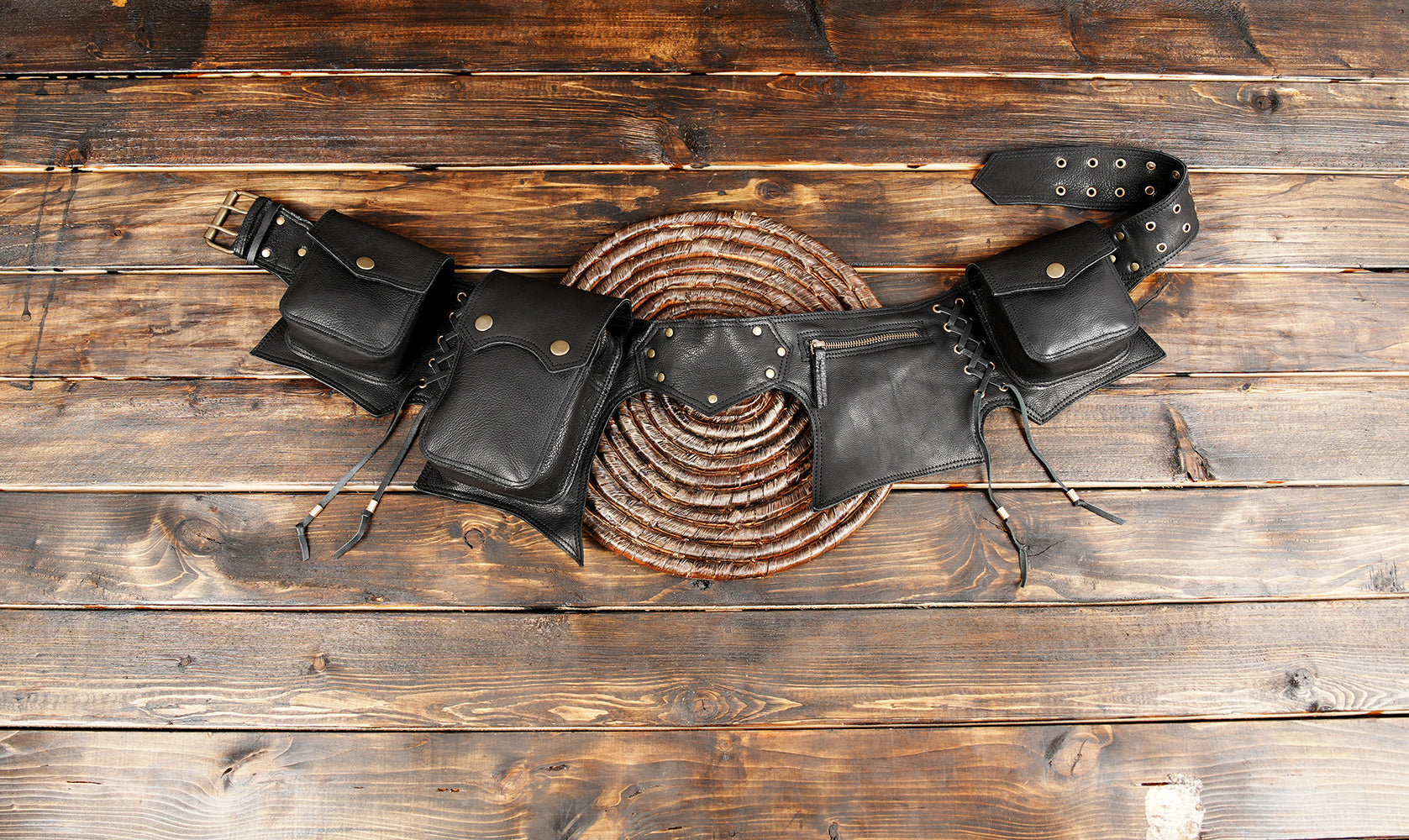 Handmade black leather utility belt bag with brass studs on wooden background