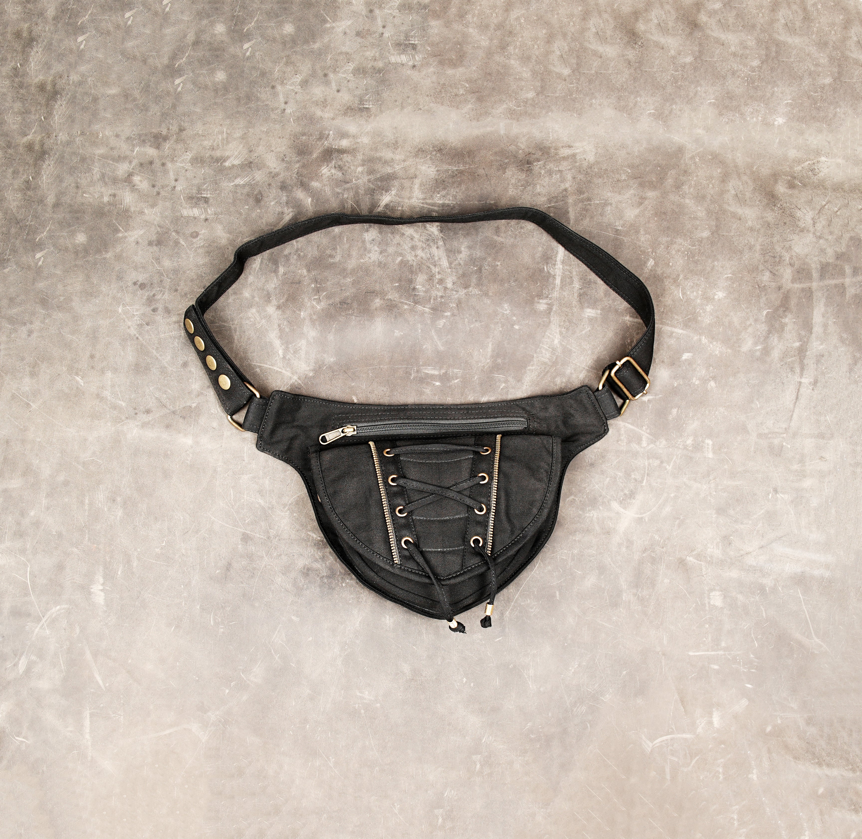 Detail shot of a matte black canvas fanny pack worn on the hip, featuring intricate corset lacing, secure zippers, and an adjustable strap.