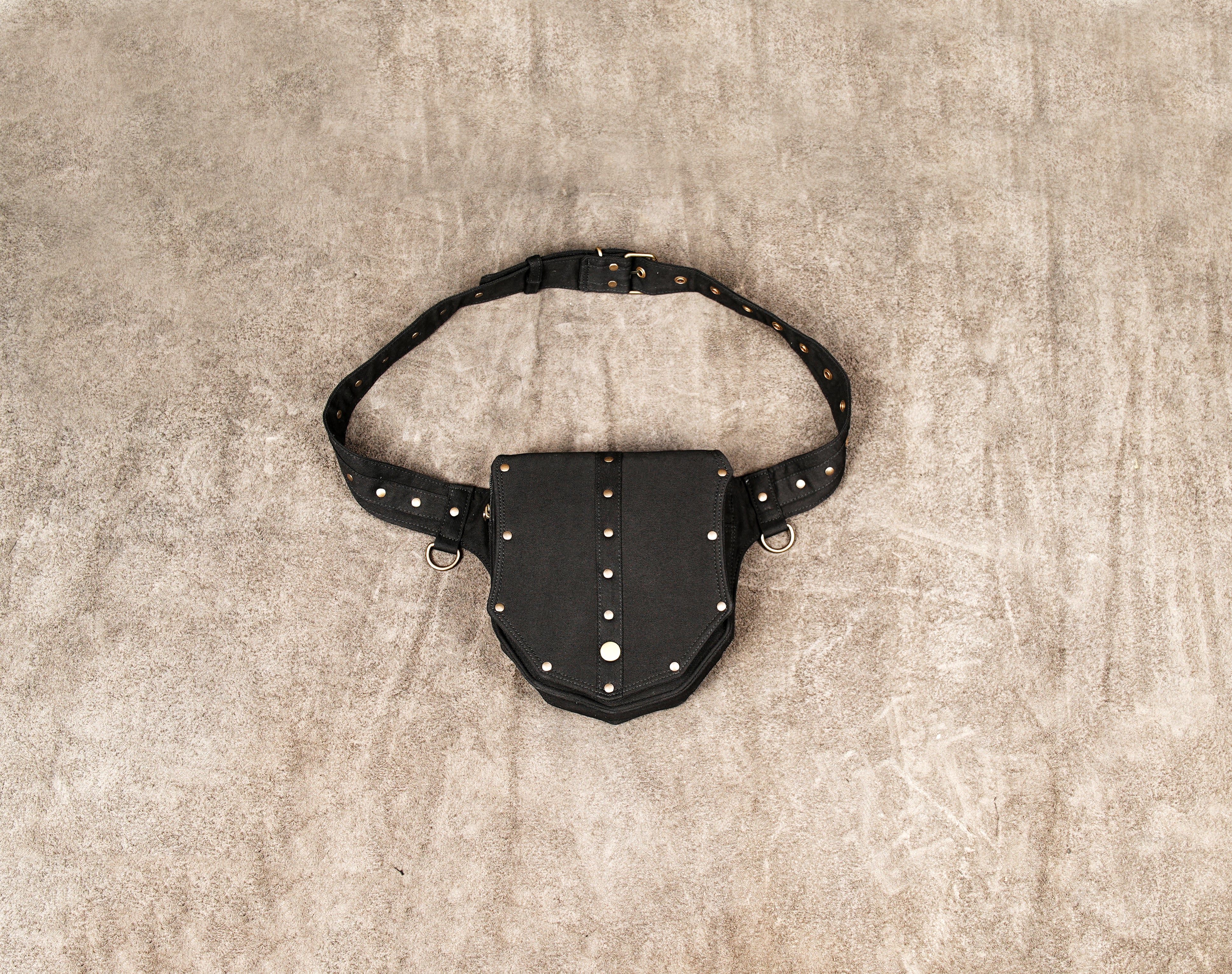 A black canvas hip bag designed for festivals, showing the side release buckle, adjustable strap length, and attached antique brass D-ring for keys.