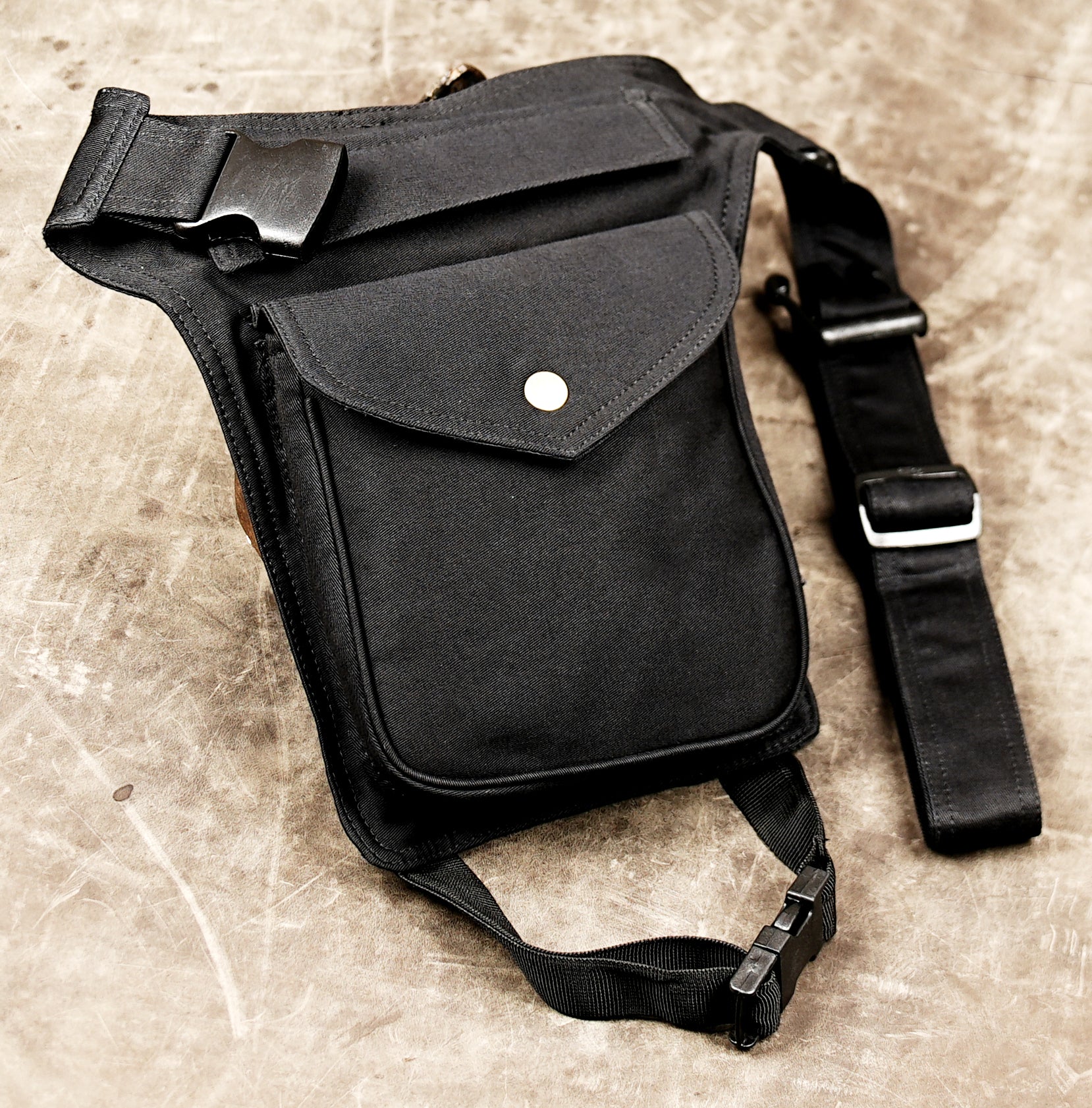 Black canvas belt bag with brass button pocket for phone and wallet.