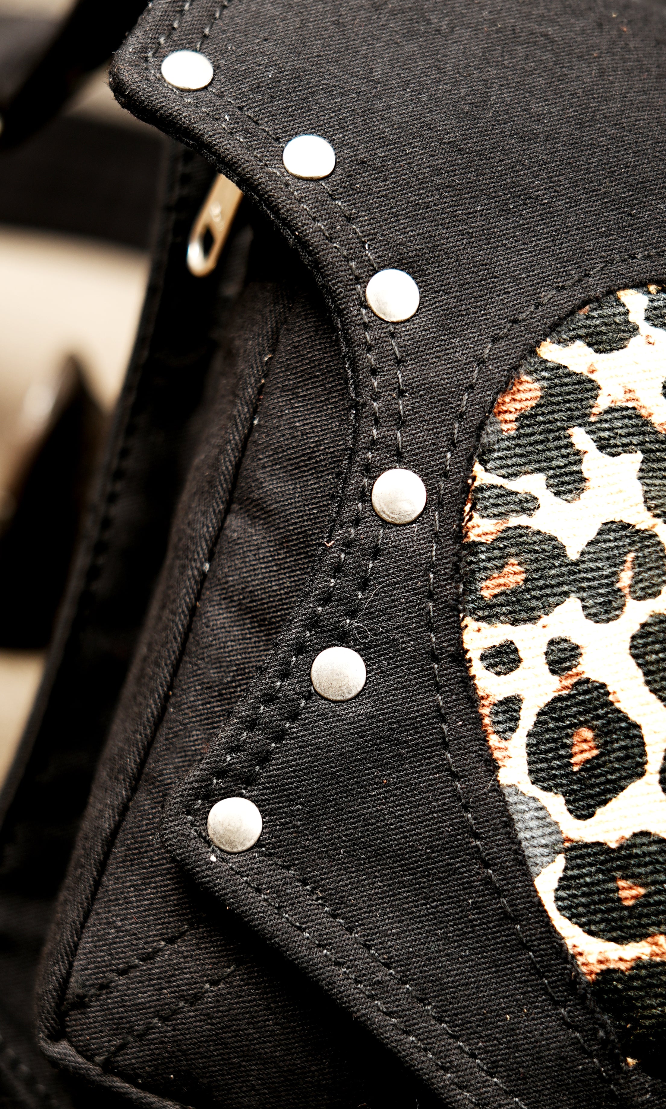 Multiple metal rivets line the edges and straps of this black fabric thigh bag accessory.