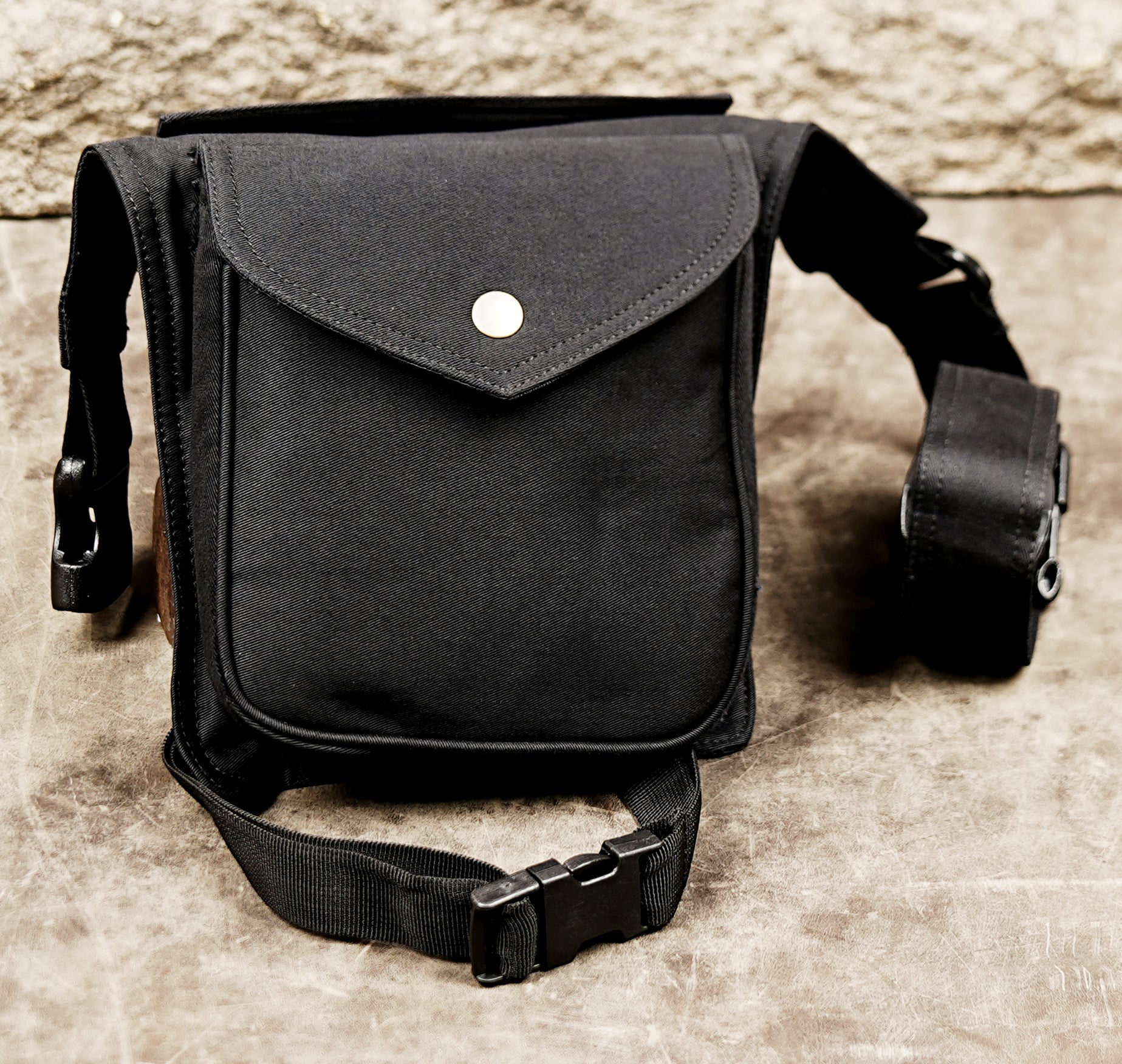 Black thigh bag with flap pocket, brass snap button, and quick release buckle