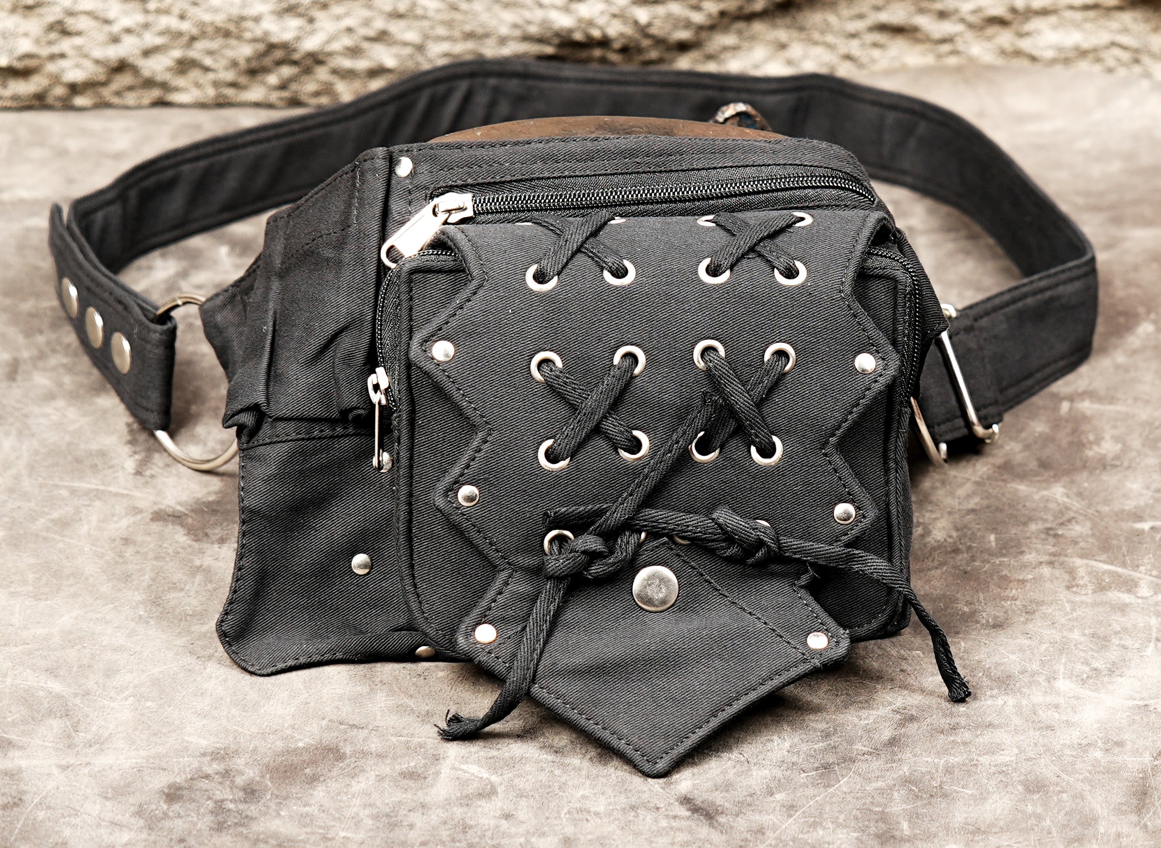 Steampunk-inspired utility waist bag with central braided detail, on concrete.