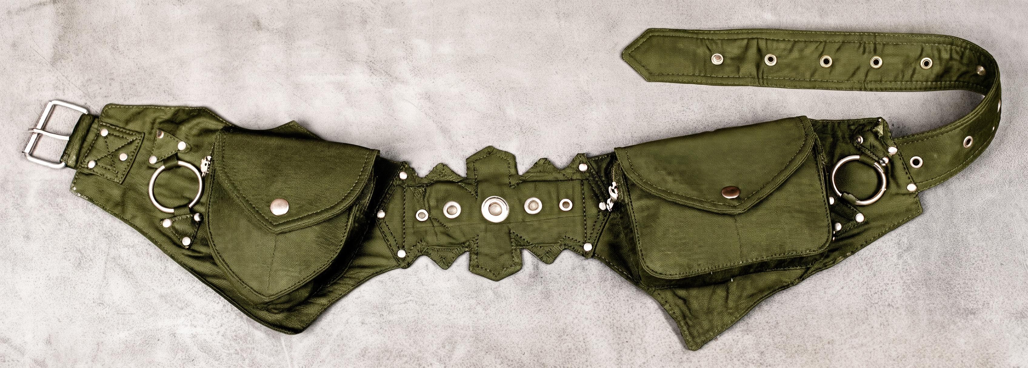 A black leather utility belt with multiple pouches, silver metal rings, studs, and a buckle, displayed flat on a textured beige background.