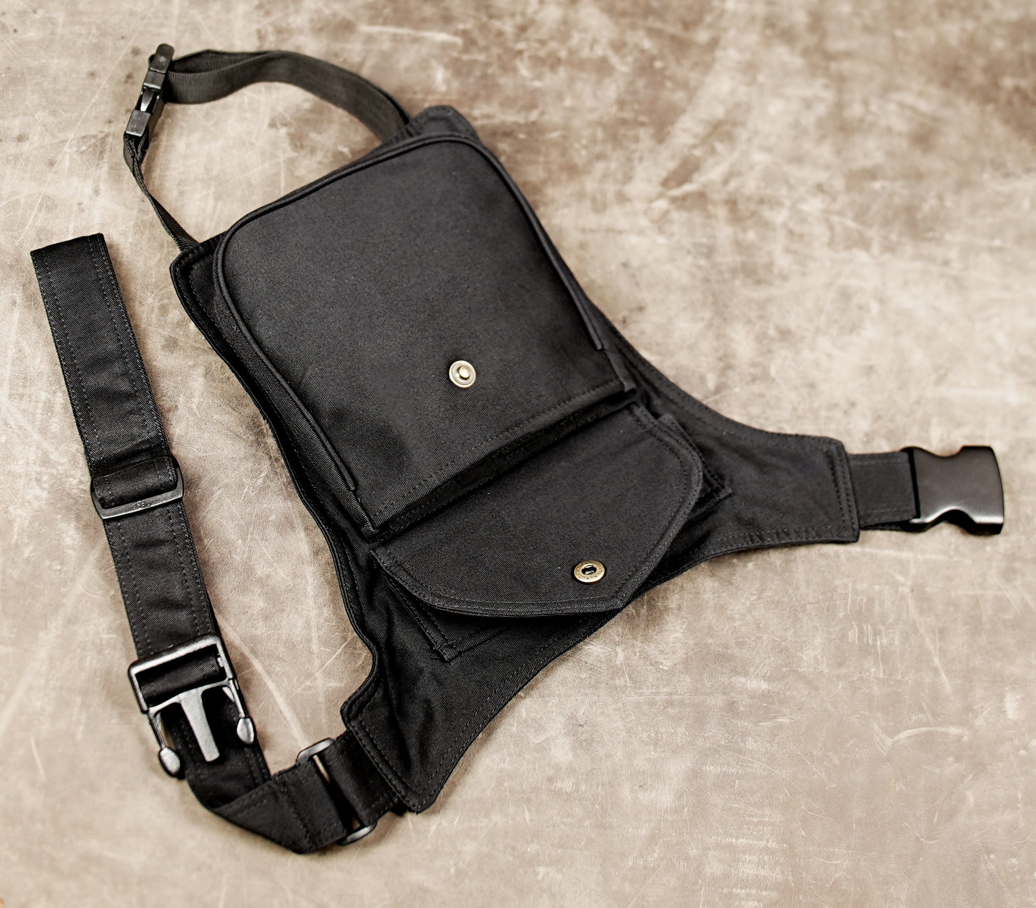 Black canvas side bag with adjustable strap and brass snap closure.