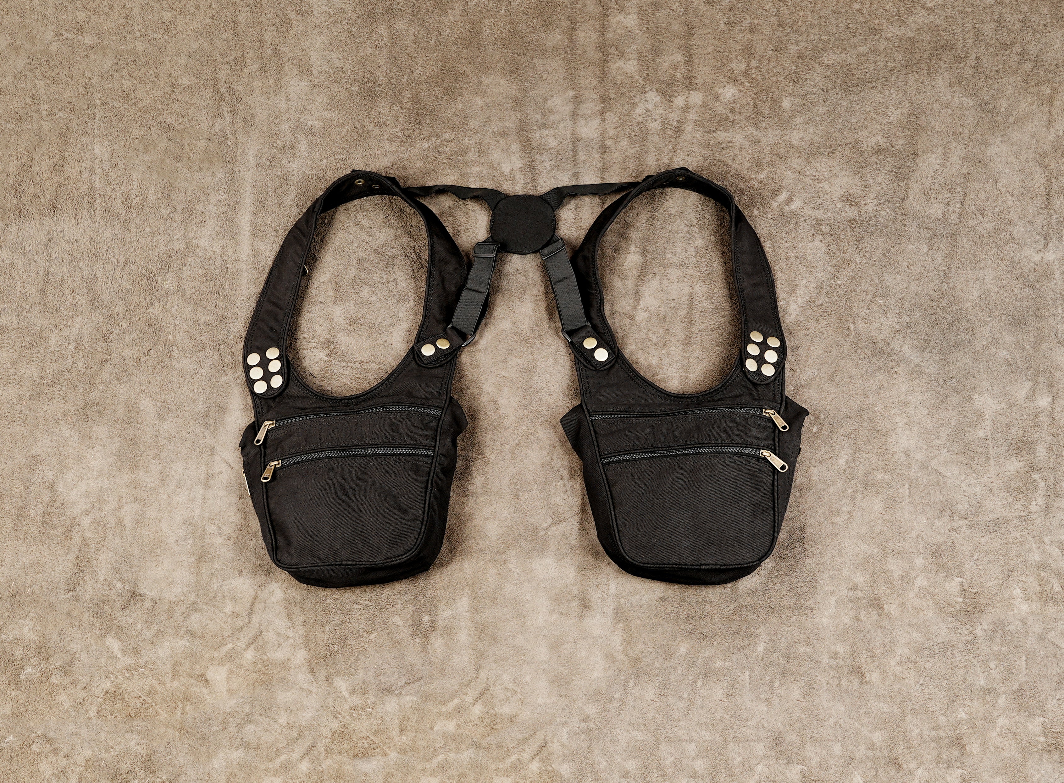 A black tactical-style harness vest with two front pouches, studded side details, and adjustable shoulder straps