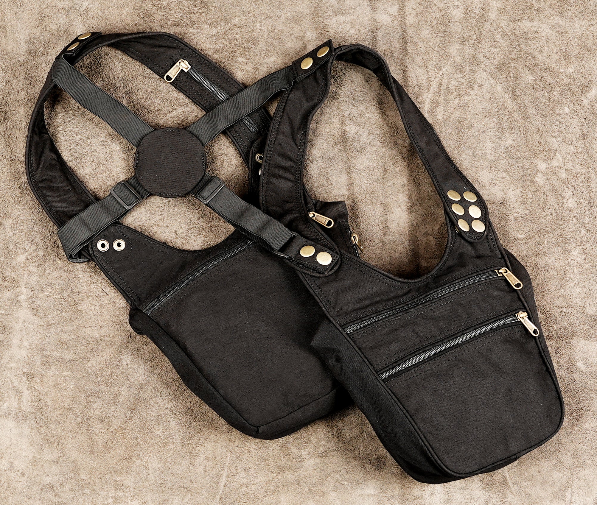 A black canvas crossbody bag with adjustable shoulder straps, gold-tone snap buttons, and multiple zippered pockets