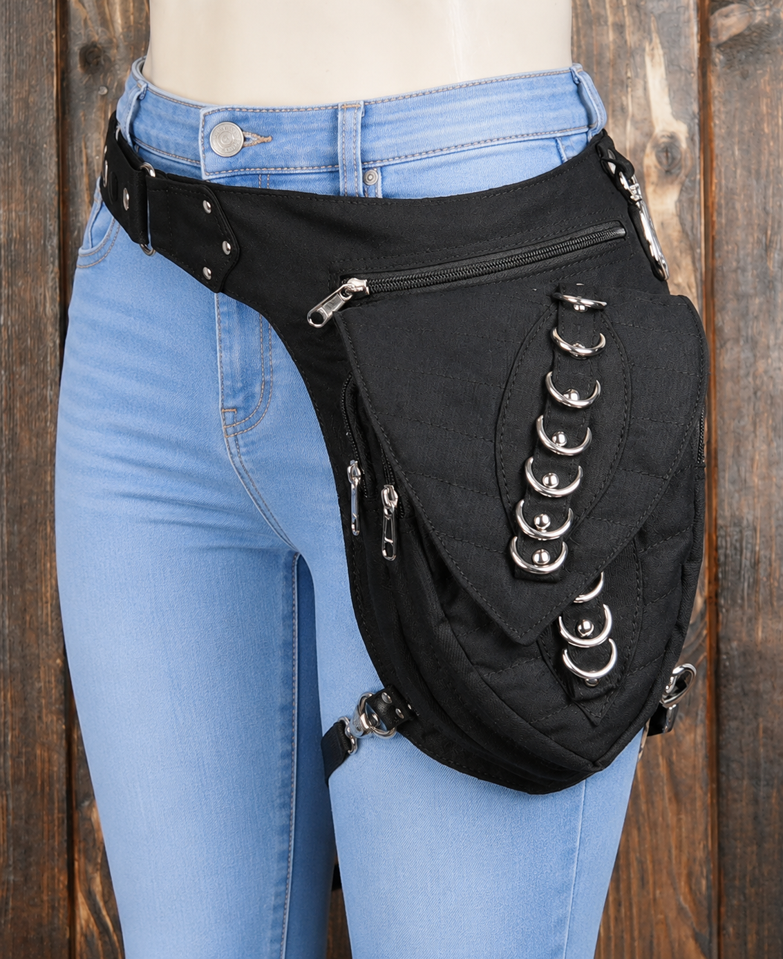 Studded canvas drop leg bag with zipper pouch on wood background.