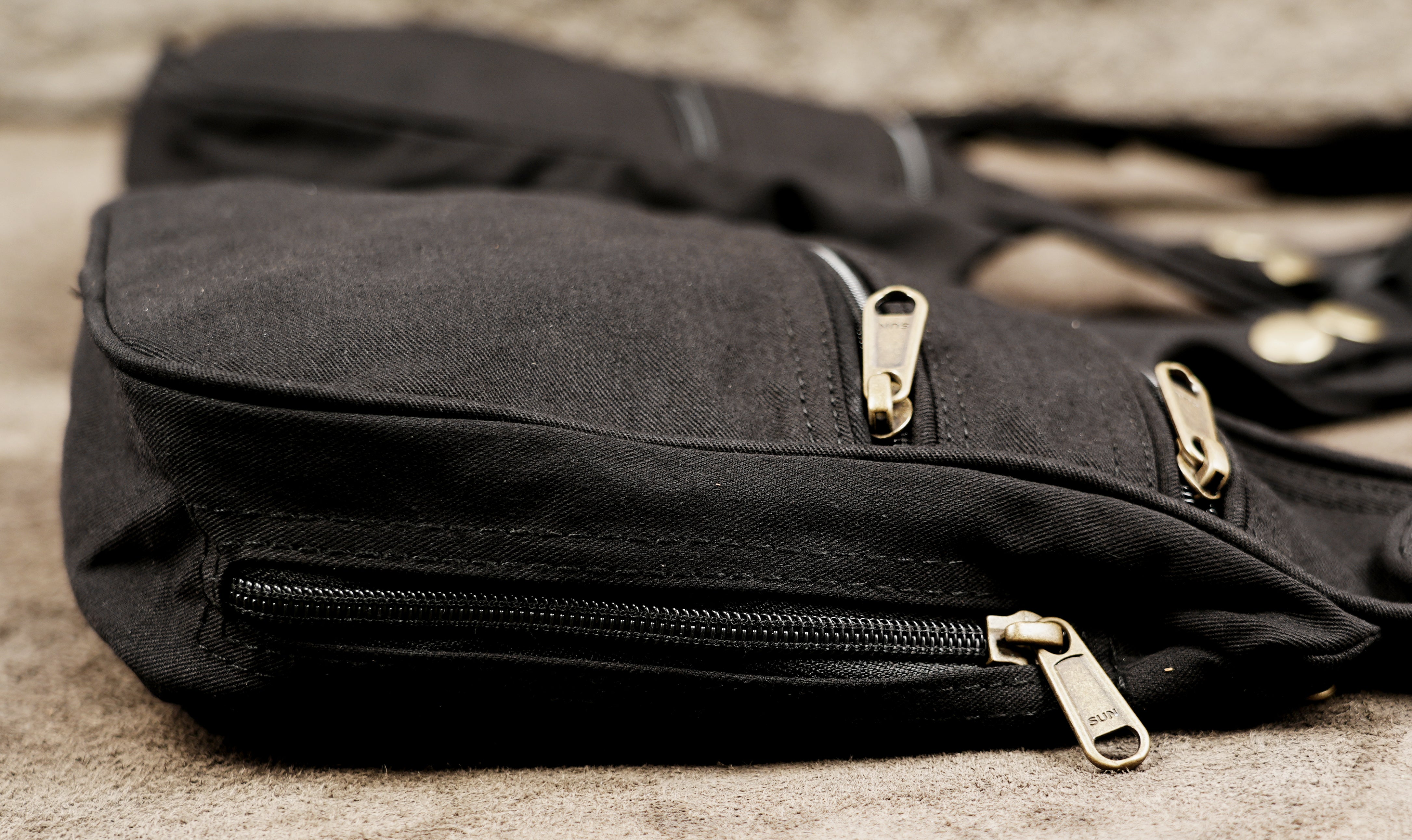 A close-up of a black canvas crossbody bag with gold-toned metal zippers