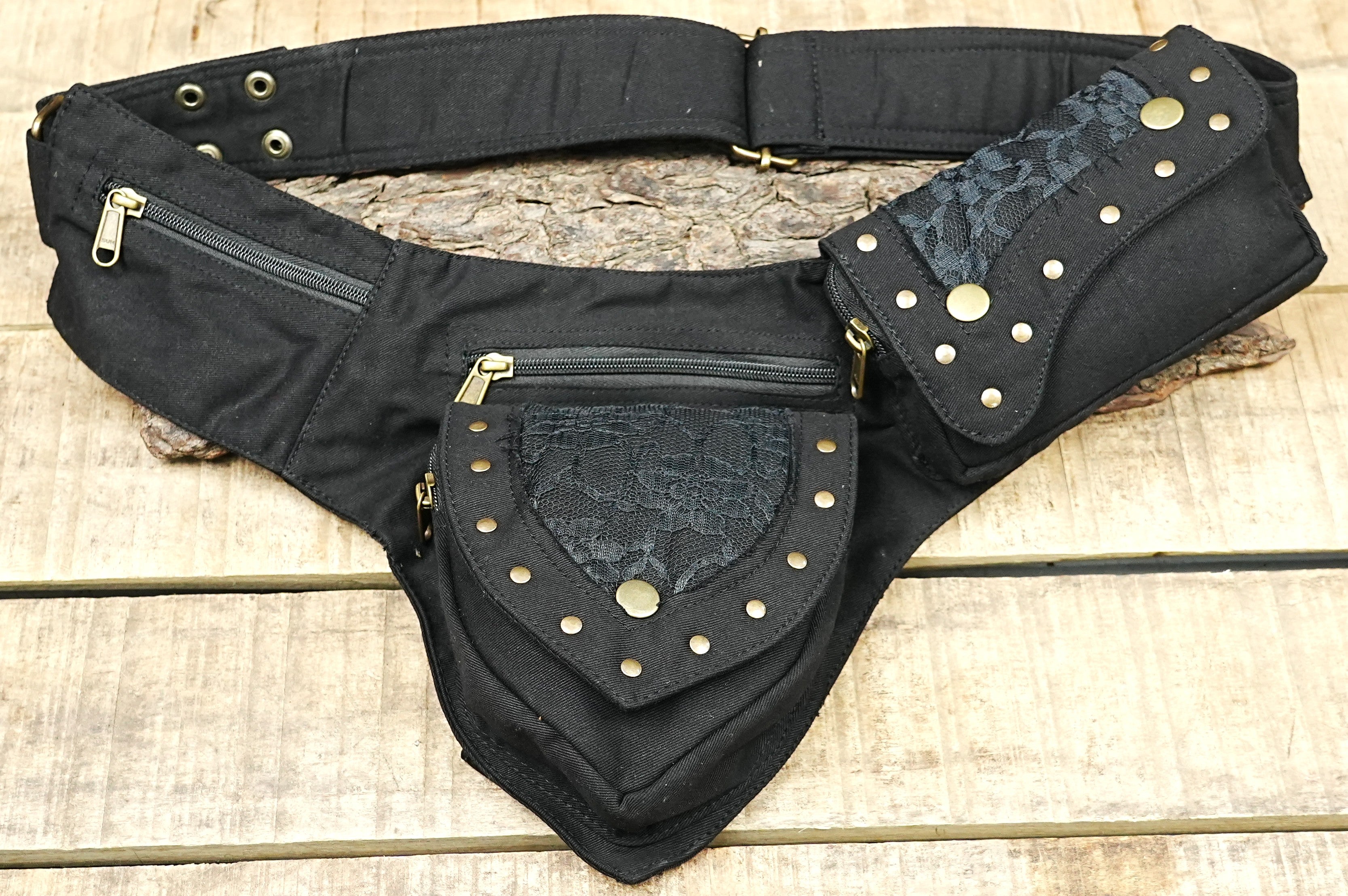 Handmade canvas pixie utility belt with dark lace overlay and brass studs laid flat on wood