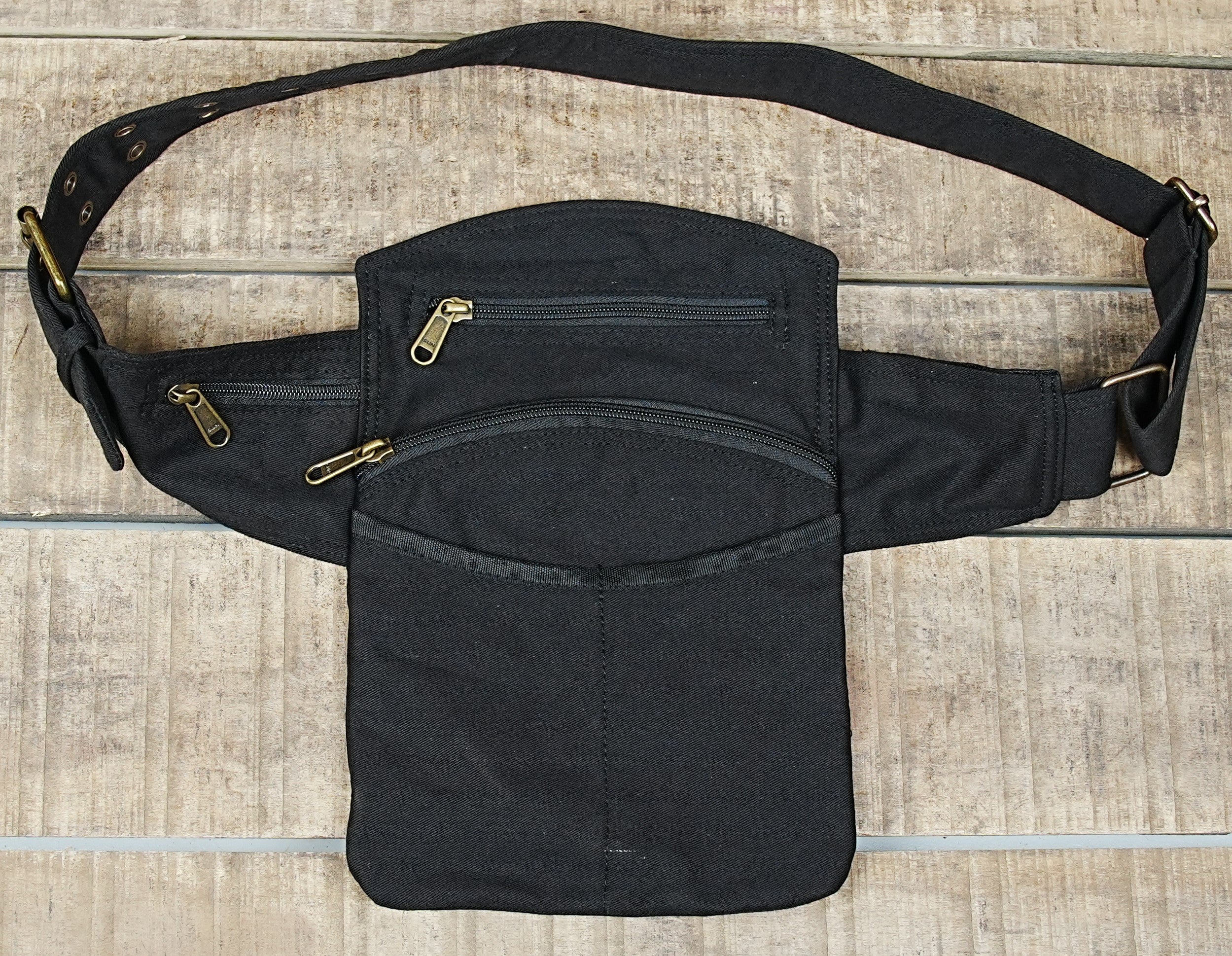 Black canvas utility belt with multiple zippered pockets on wooden background