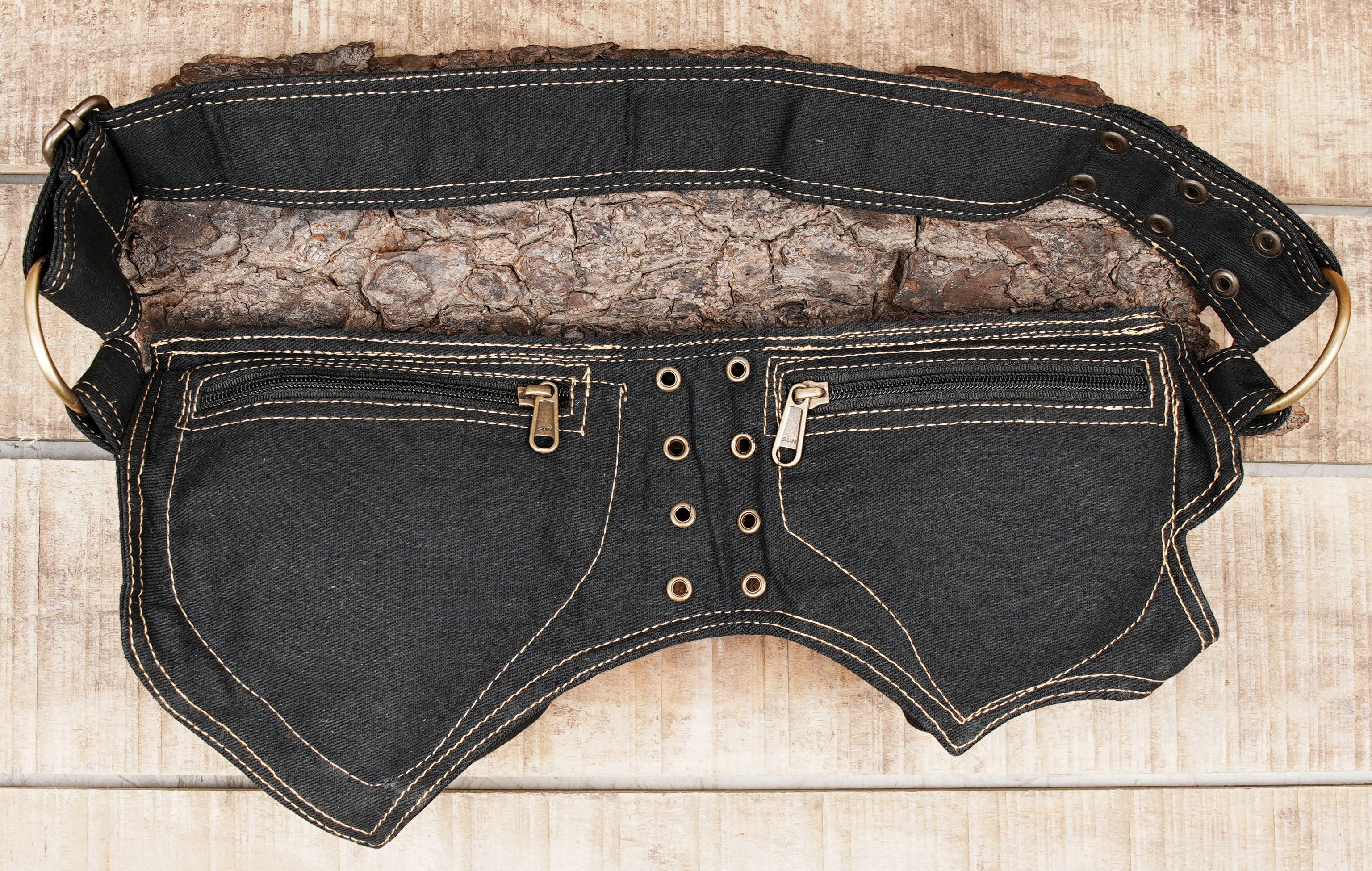 Flat lay of black canvas bum bag with brass hardware on weathered wood