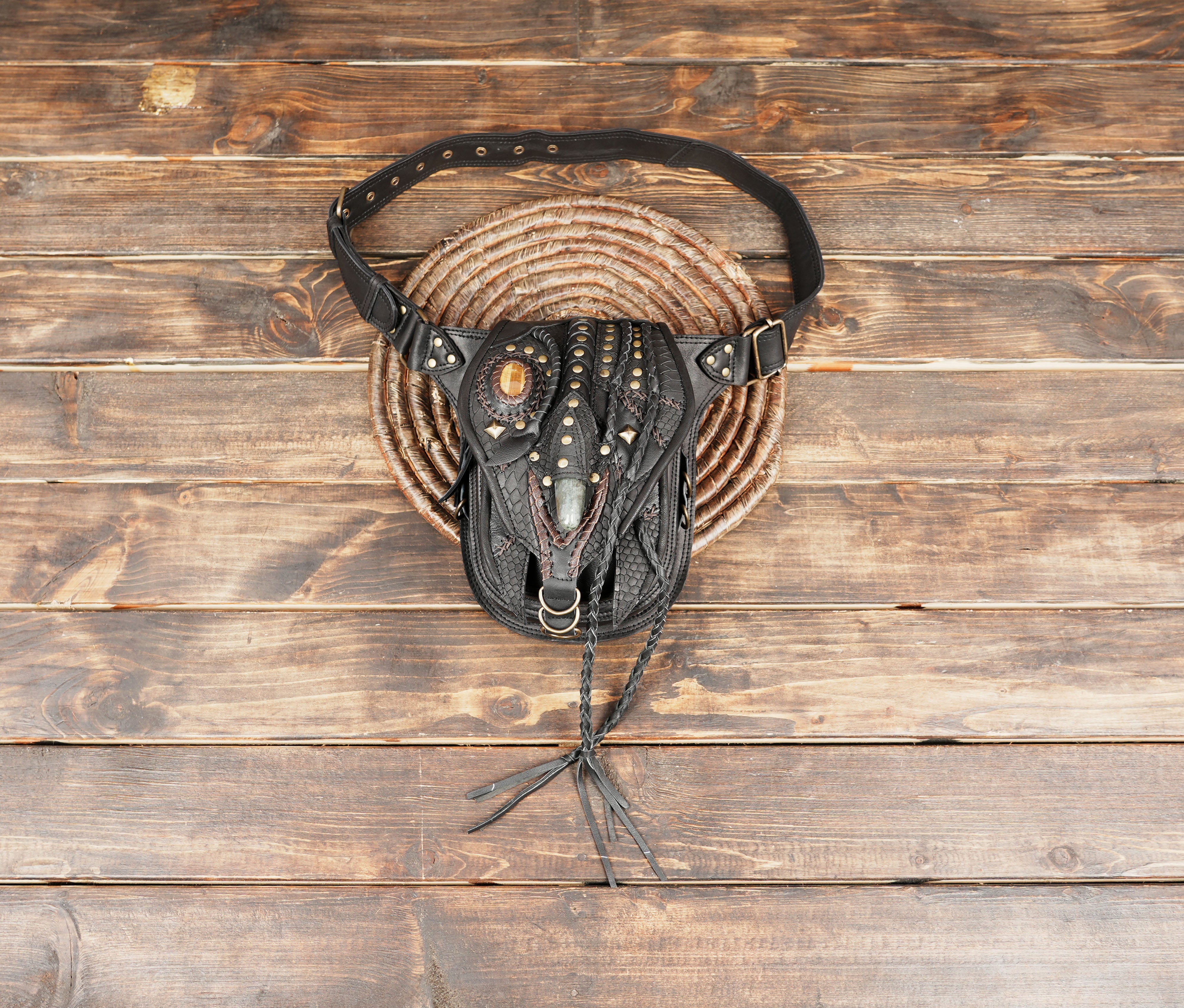 Handcrafted black leather hip bag with gemstone accent on wooden background