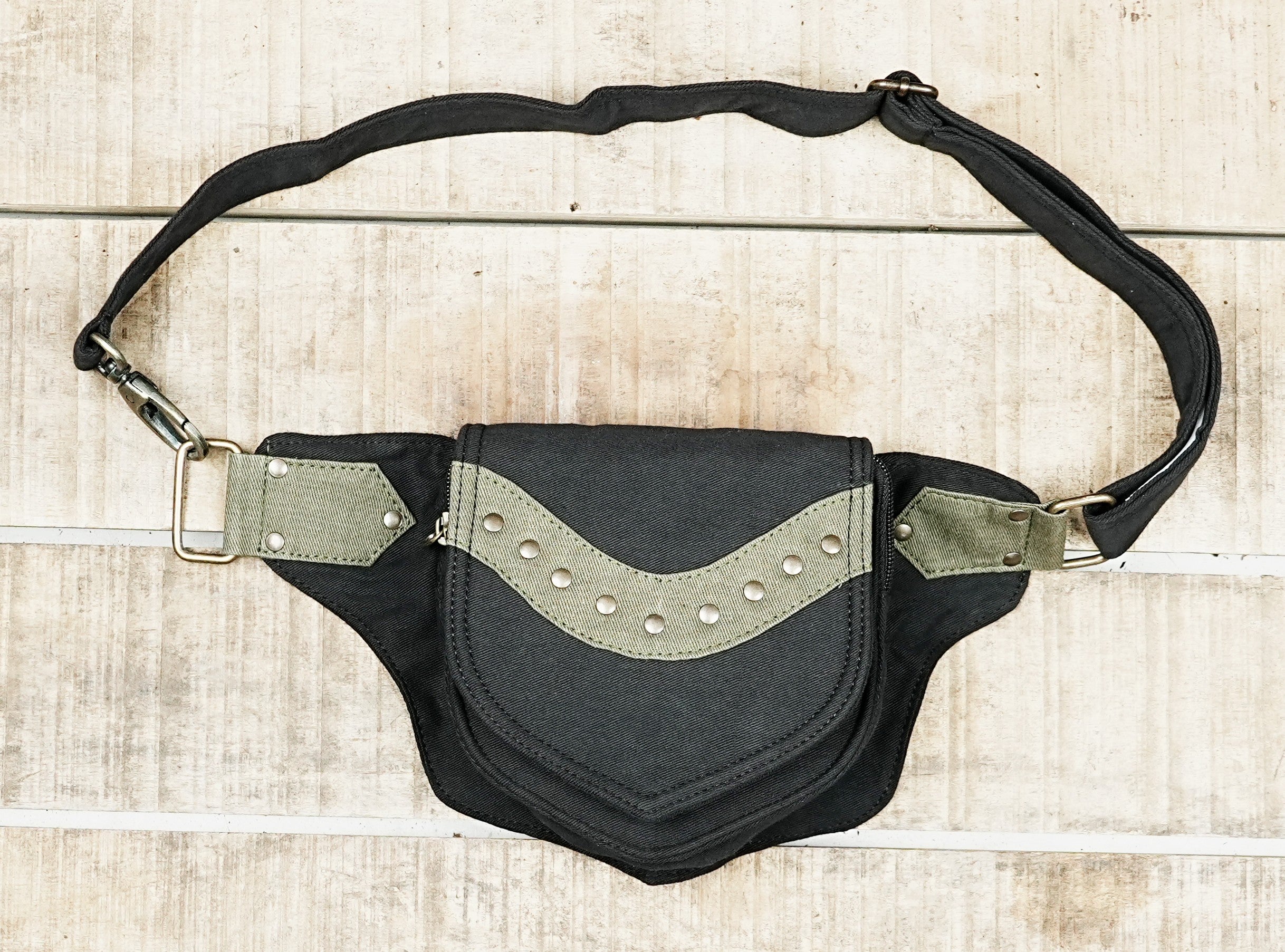 Handmade black canvas utility belt with olive green studded trim laid flat on wood