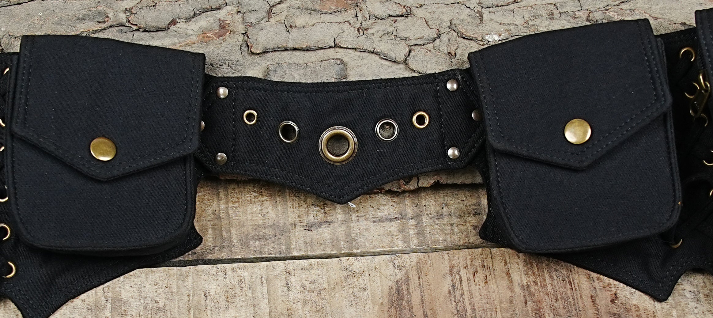 Multi-pocket festival bum bag with brass grommets on rustic wood background