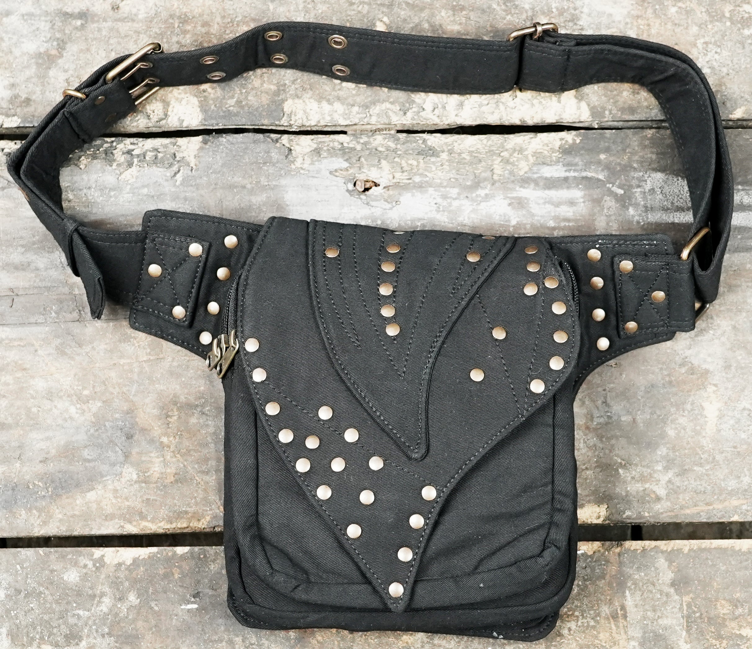 Handmade black canvas pixie utility belt with brass dome studs laid flat on wood