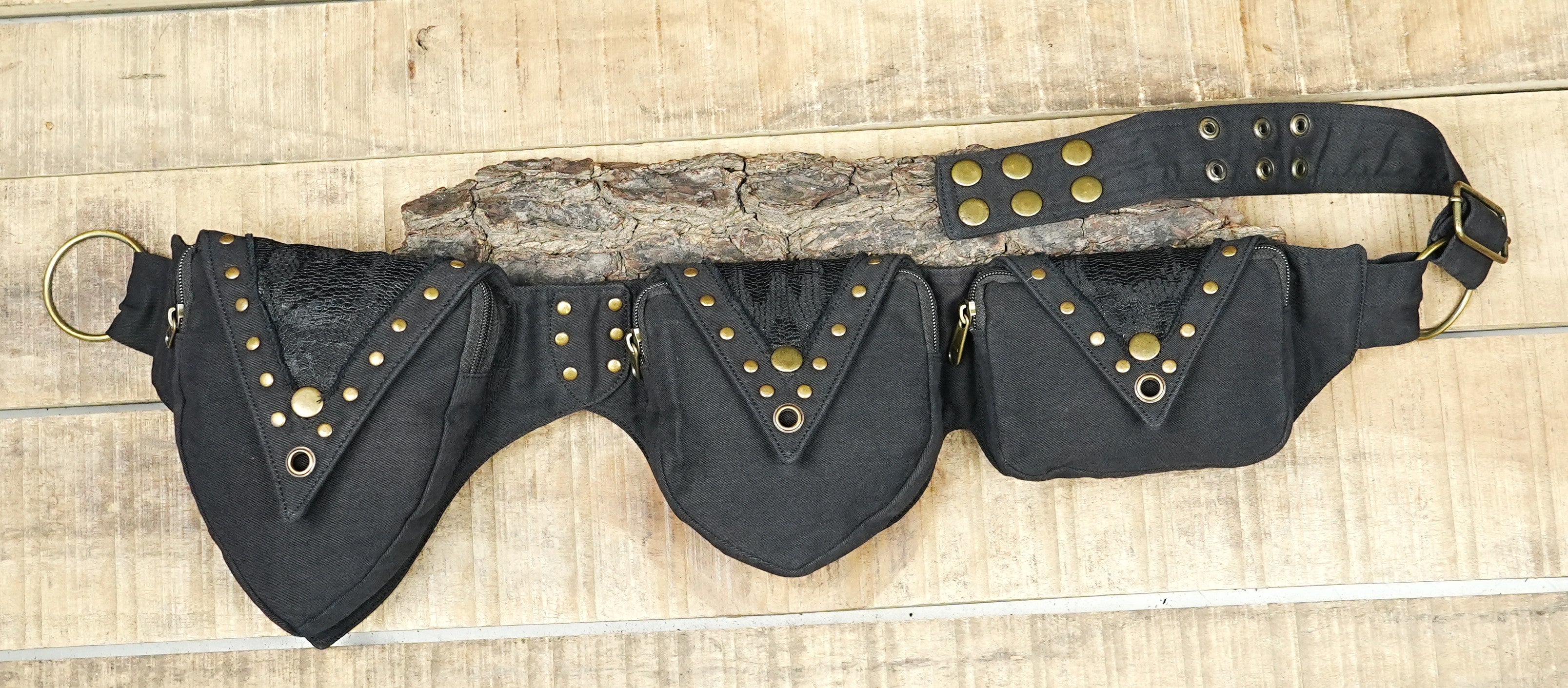 Handmade canvas utility belt with three pointed studded pockets laid flat on wood