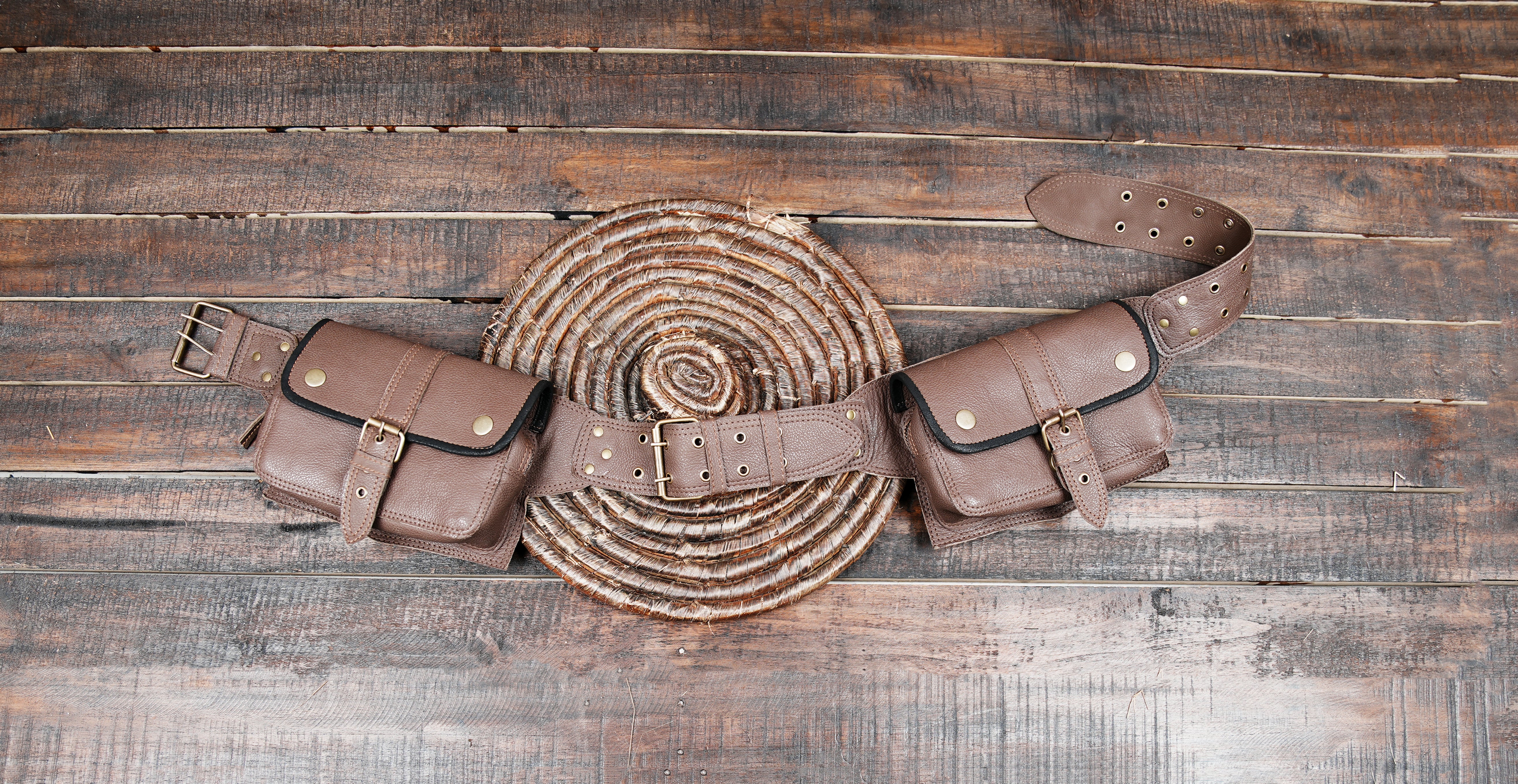 Brown leather utility belt bag with two pouches and brass buckles on rustic wooden background