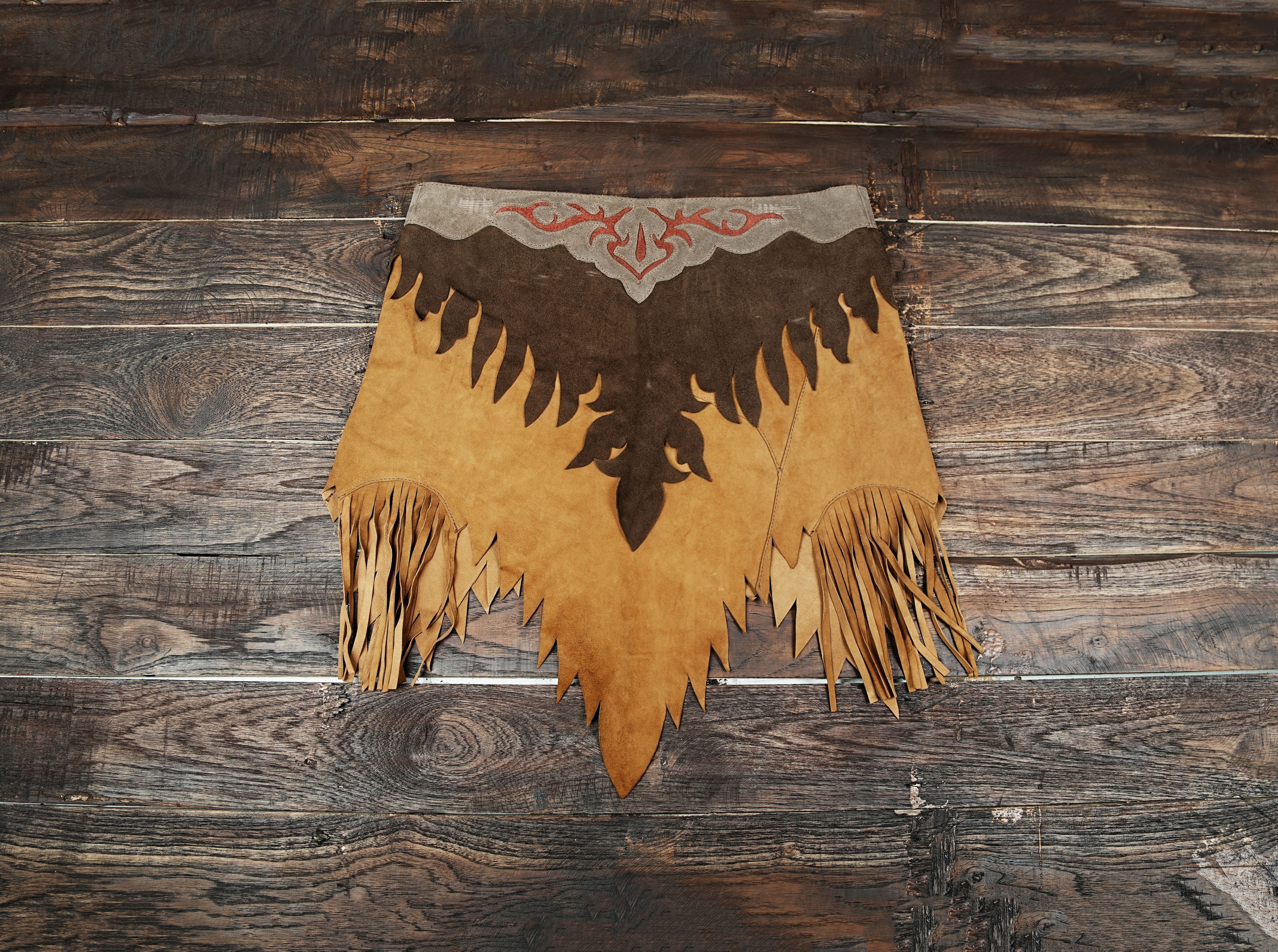 Handmade western leather skirt with fringe and embroidered design on wood background