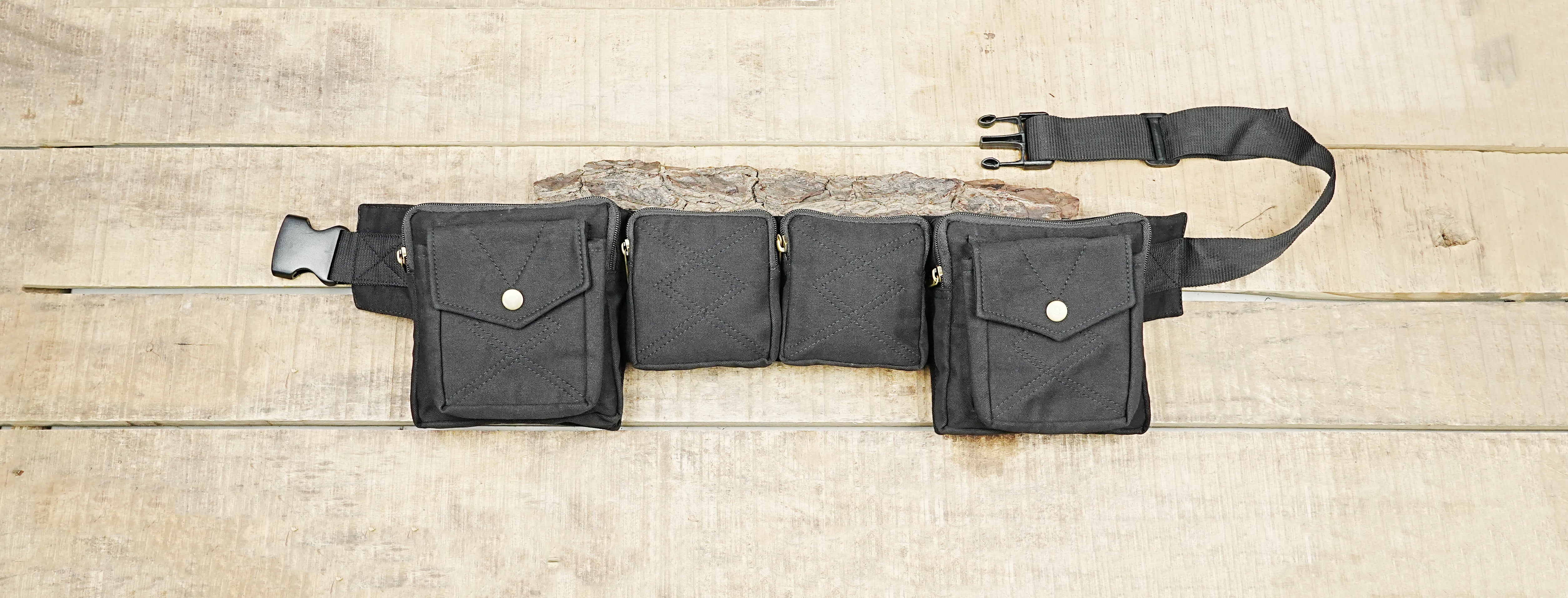 Handmade black canvas utility belt with four front pockets on wooden surface