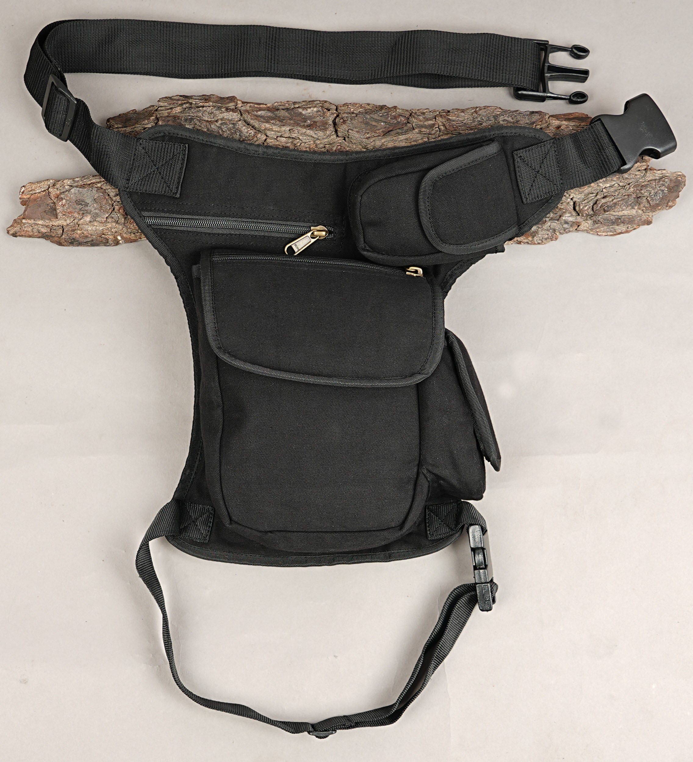 Handmade black cotton canvas drop leg bag with multi-pocket layout laid flat on rustic wood.
