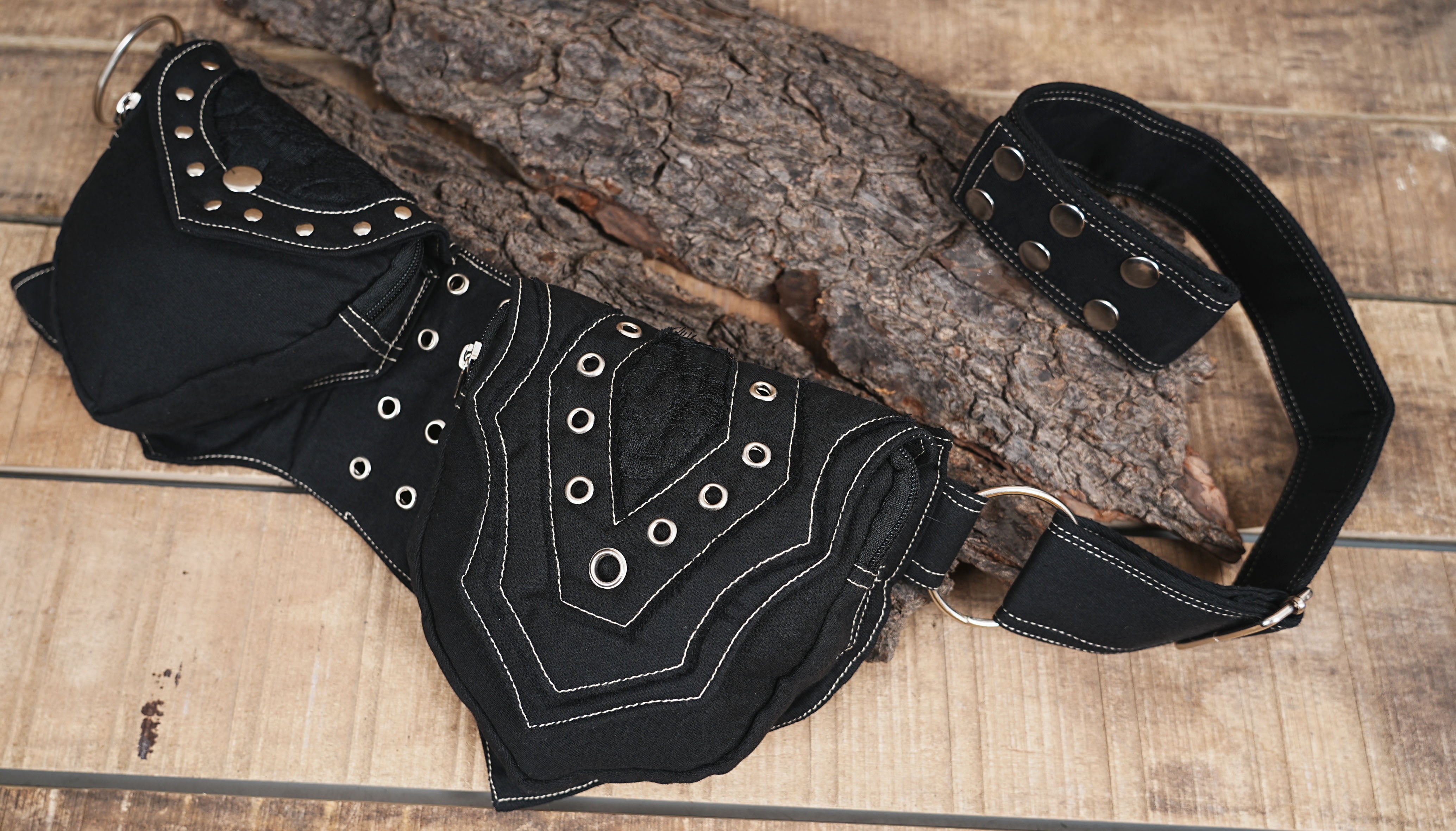 Detailed close-up of a black canvas hip bag with ornate stitching and metal decorative rings.