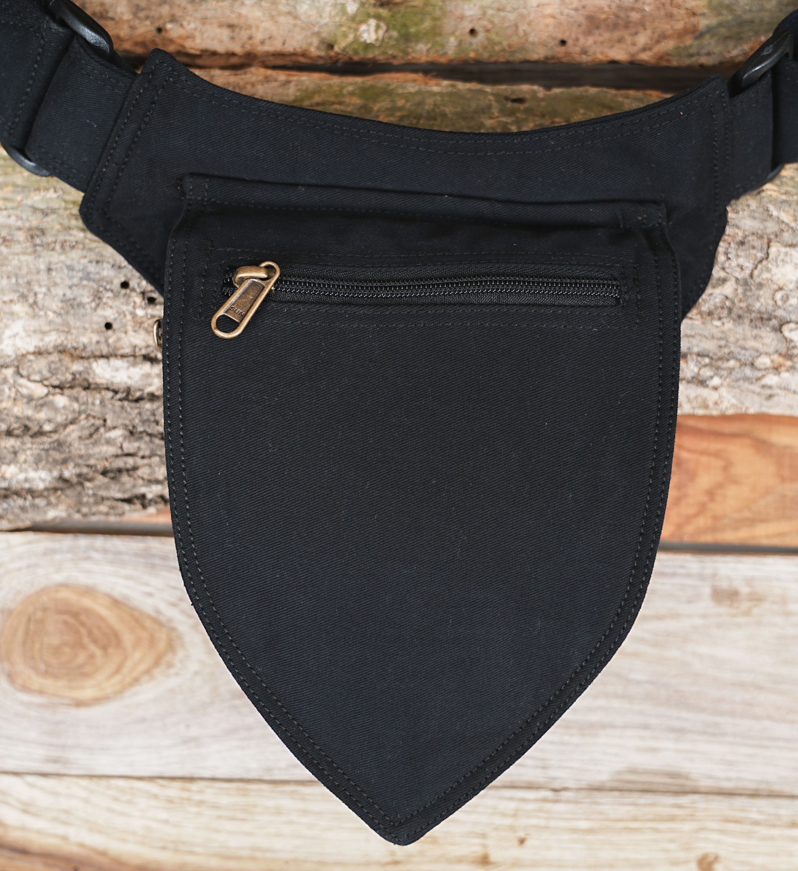 Adjustable black canvas hip bag laid on wooden log background