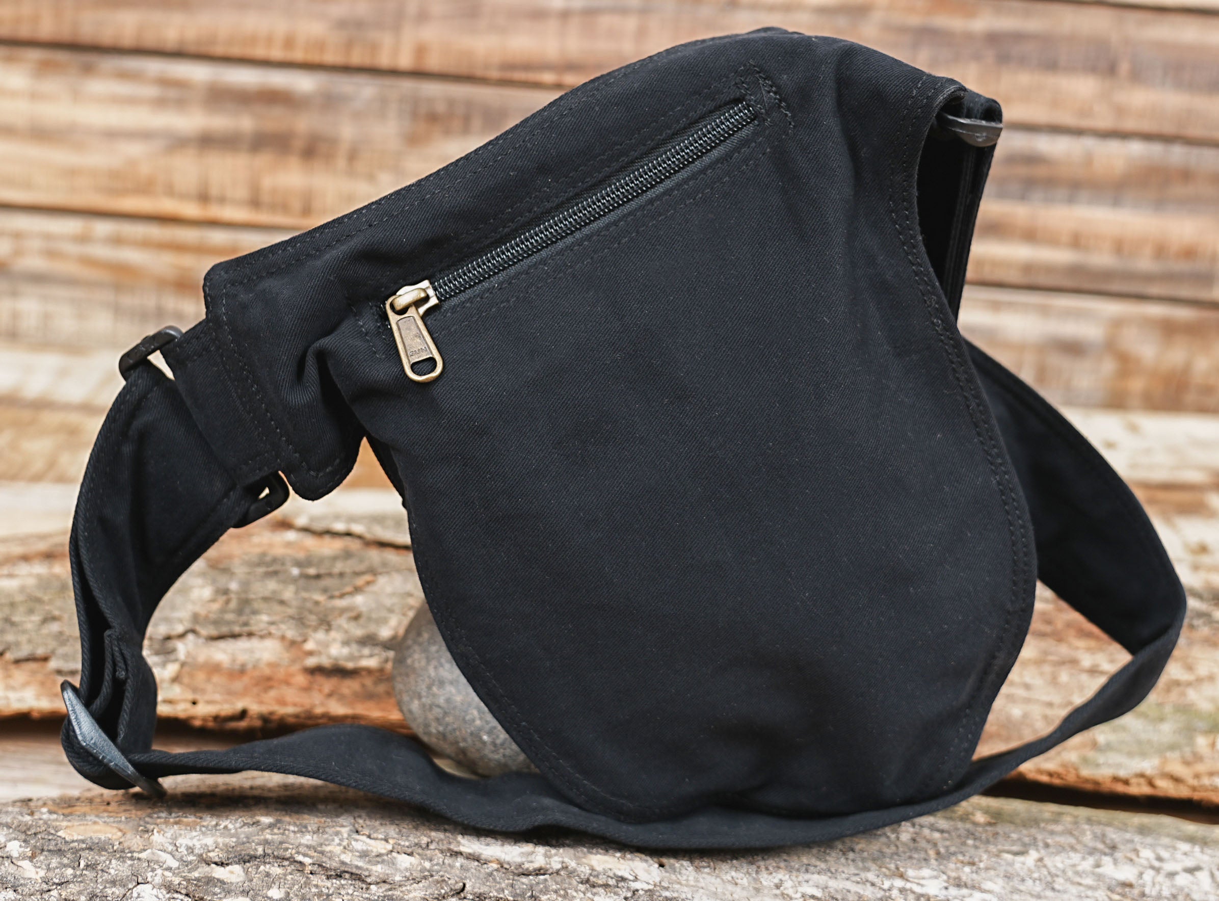 Black canvas waist bag laid flat on rustic wood surface
