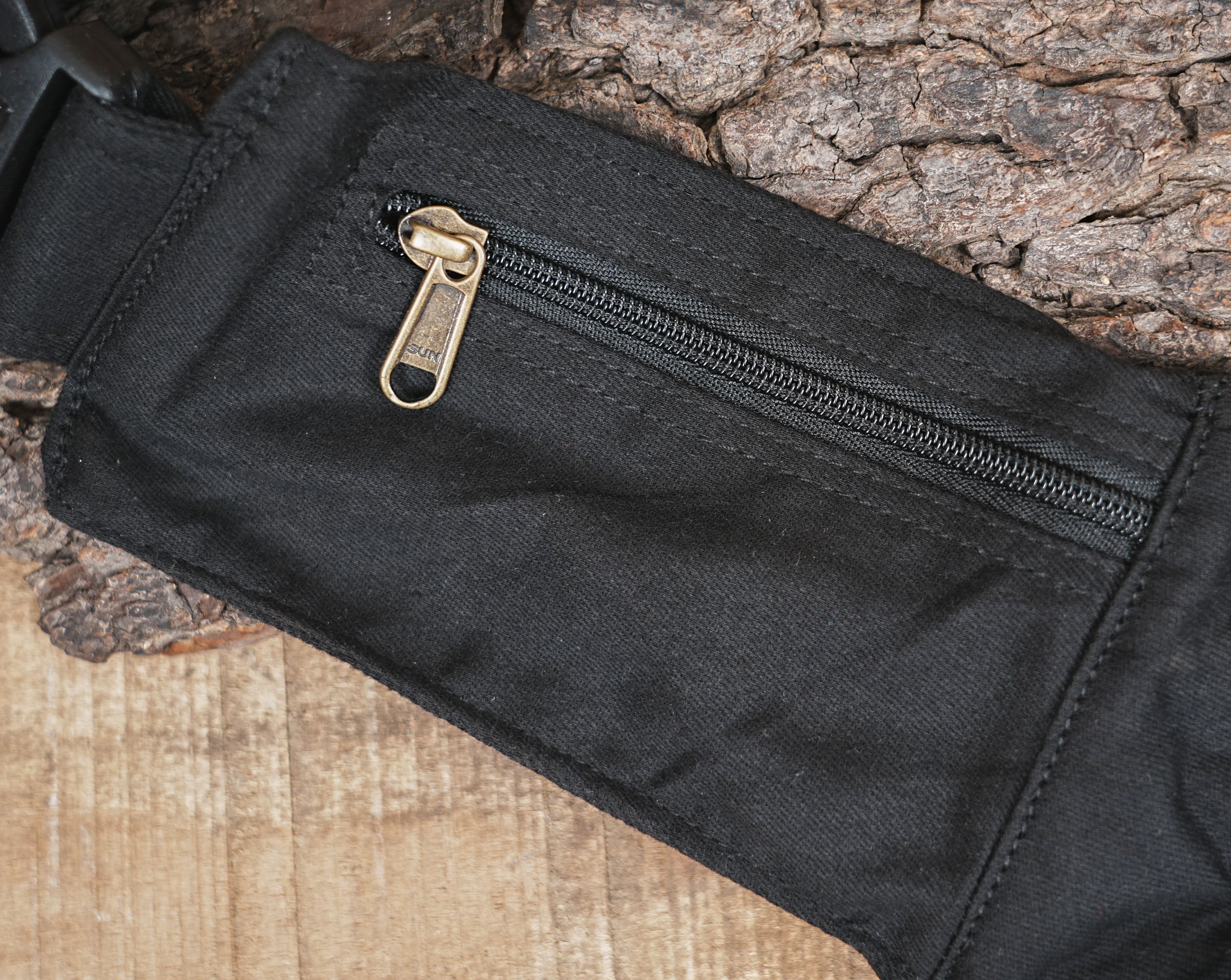 Product photo of a unisex black utility pouch with a geometric flap and sturdy brass buckles, resting on a wooden background.
