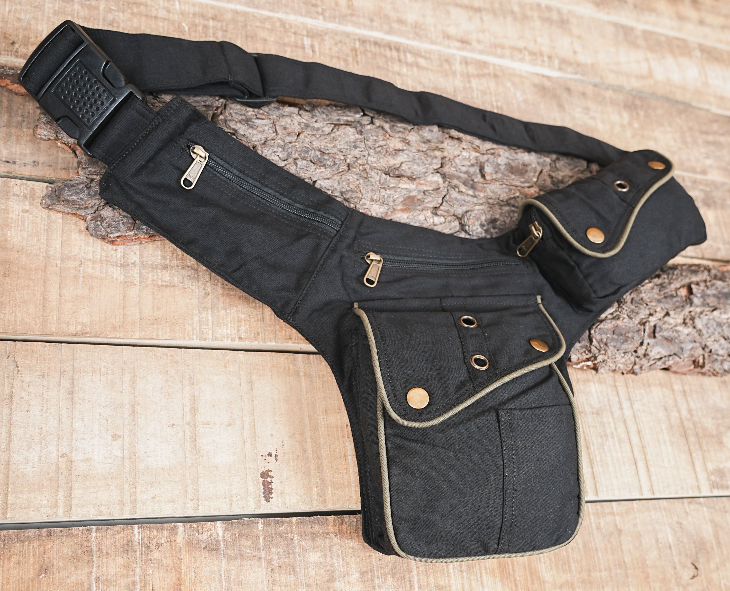 Detail shot of matte black canvas fanny pack worn on the hip, featuring taupe piping and aged brass hardware accents.