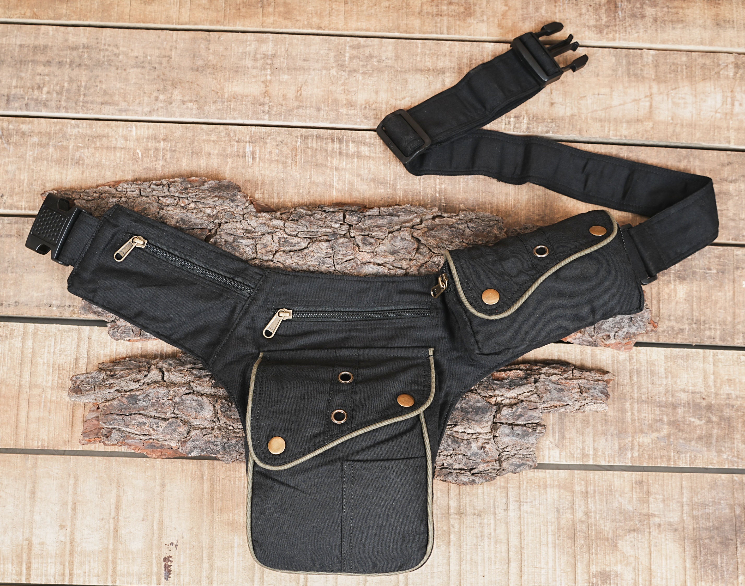 Close-up view of a black cotton canvas utility belt bag showing the multiple zippered pockets and structured front pocket with snap buttons.