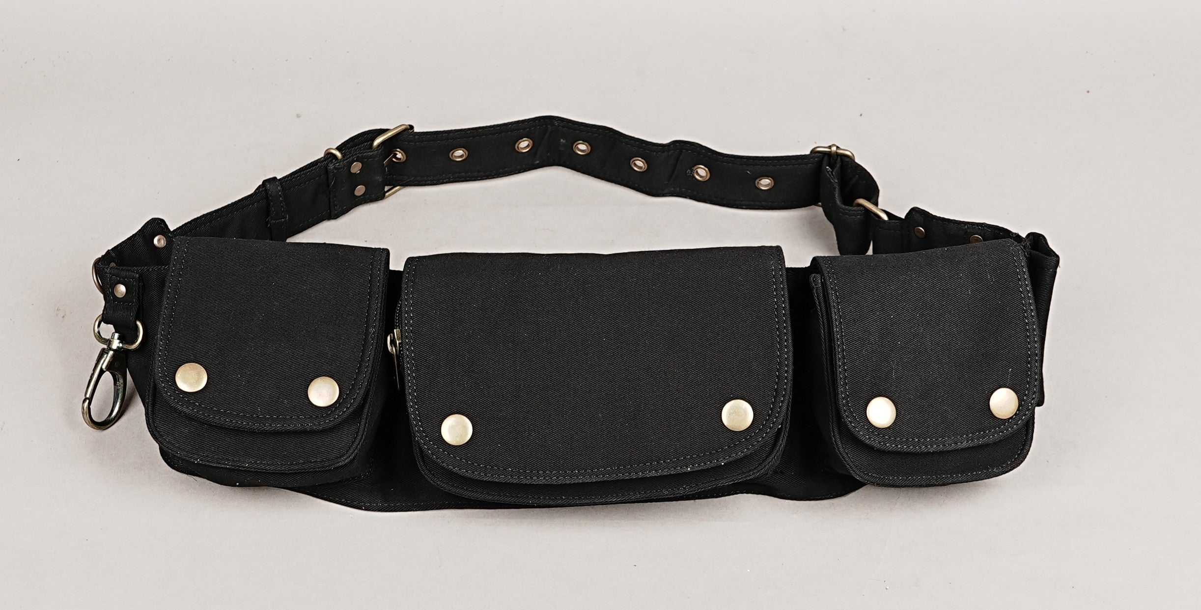 Black cotton waist belt bag with multiple pouches, brass hardware, and an adjustable strap laid flat on wood.