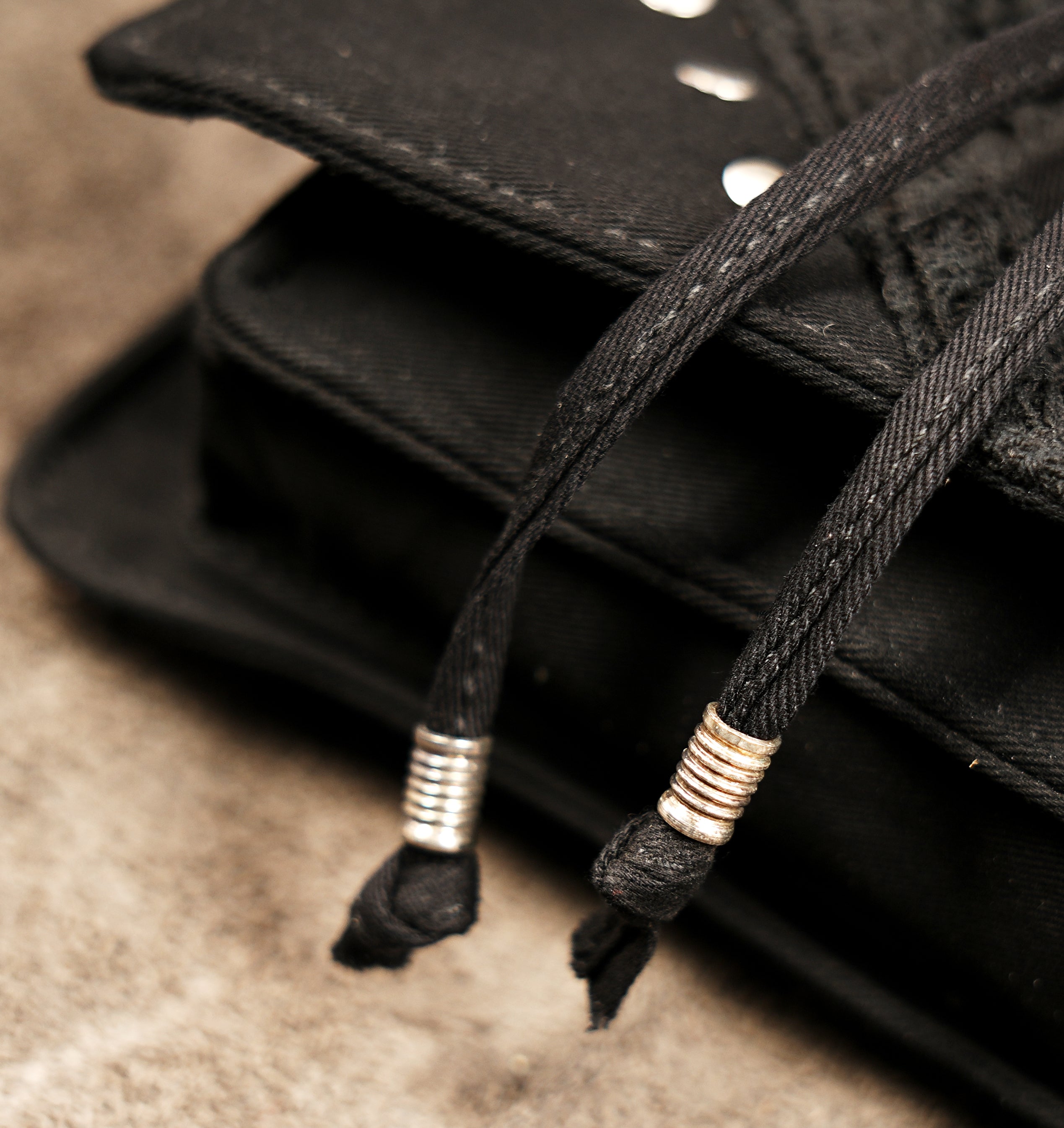 Flat lay of a black canvas waist pack showing the adjustable grommet belt and central mesh compartment.